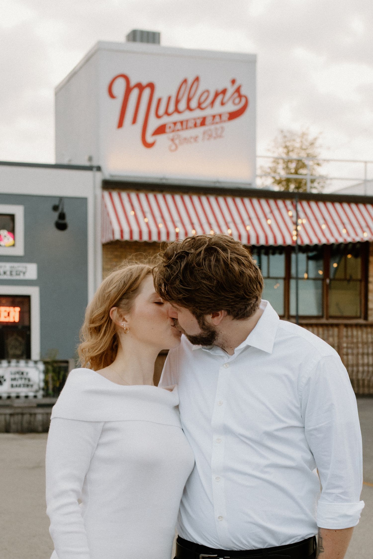 A couple in white and black attire share romantic moments outside Mullen's restaurant during Oconomowoc engagement session
