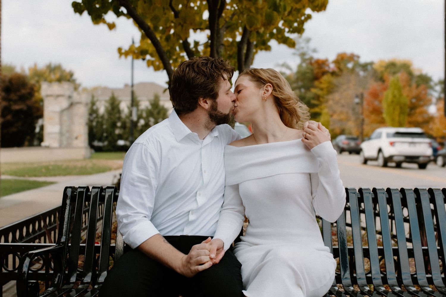 A couple embraces on a bench during an autumn day near the water in downtown Oconomowoc engagement session
