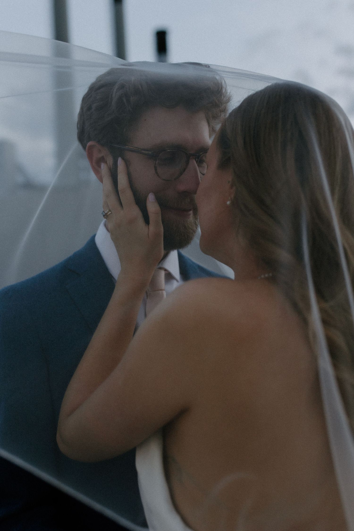 A romantic moment shared under a delicate white veil during rooftop wedding portraits