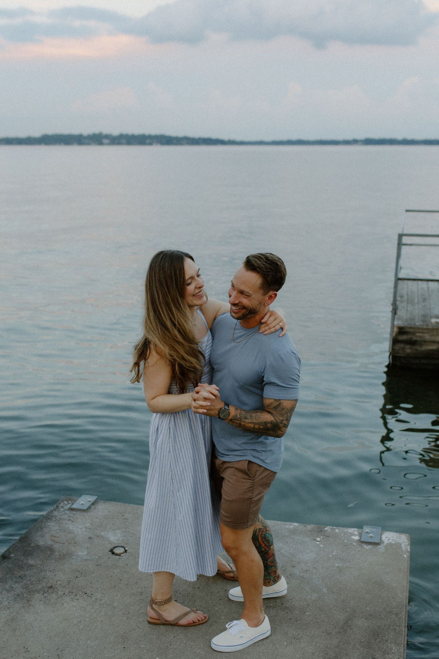 A couple shares a romantic moment on a Lake Mendota dock overlooking calm waters during blue hour engagement session
