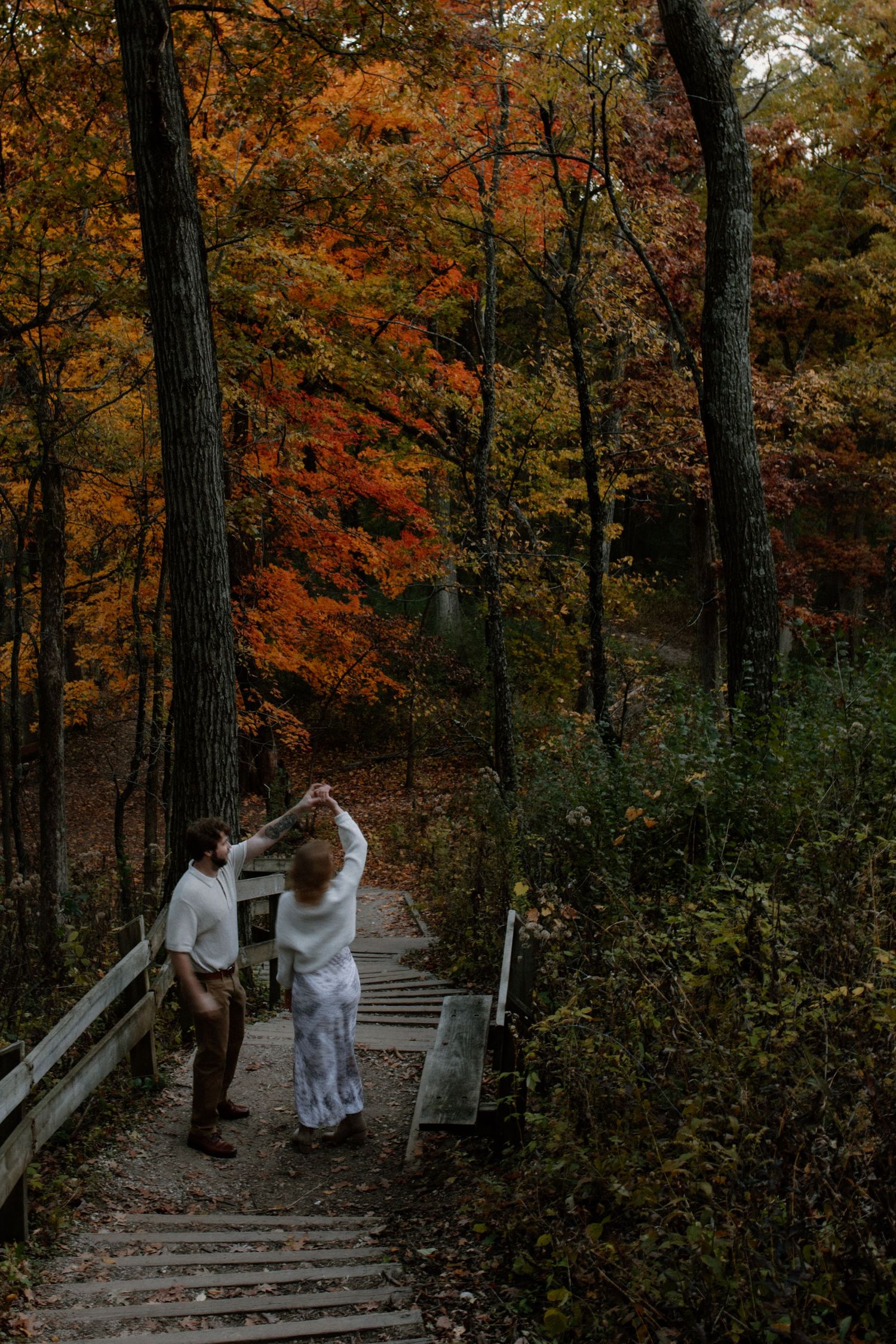 Two people dance on wooden steps surrounded by vibrant fall foliage at Lapham Peak engagement session
