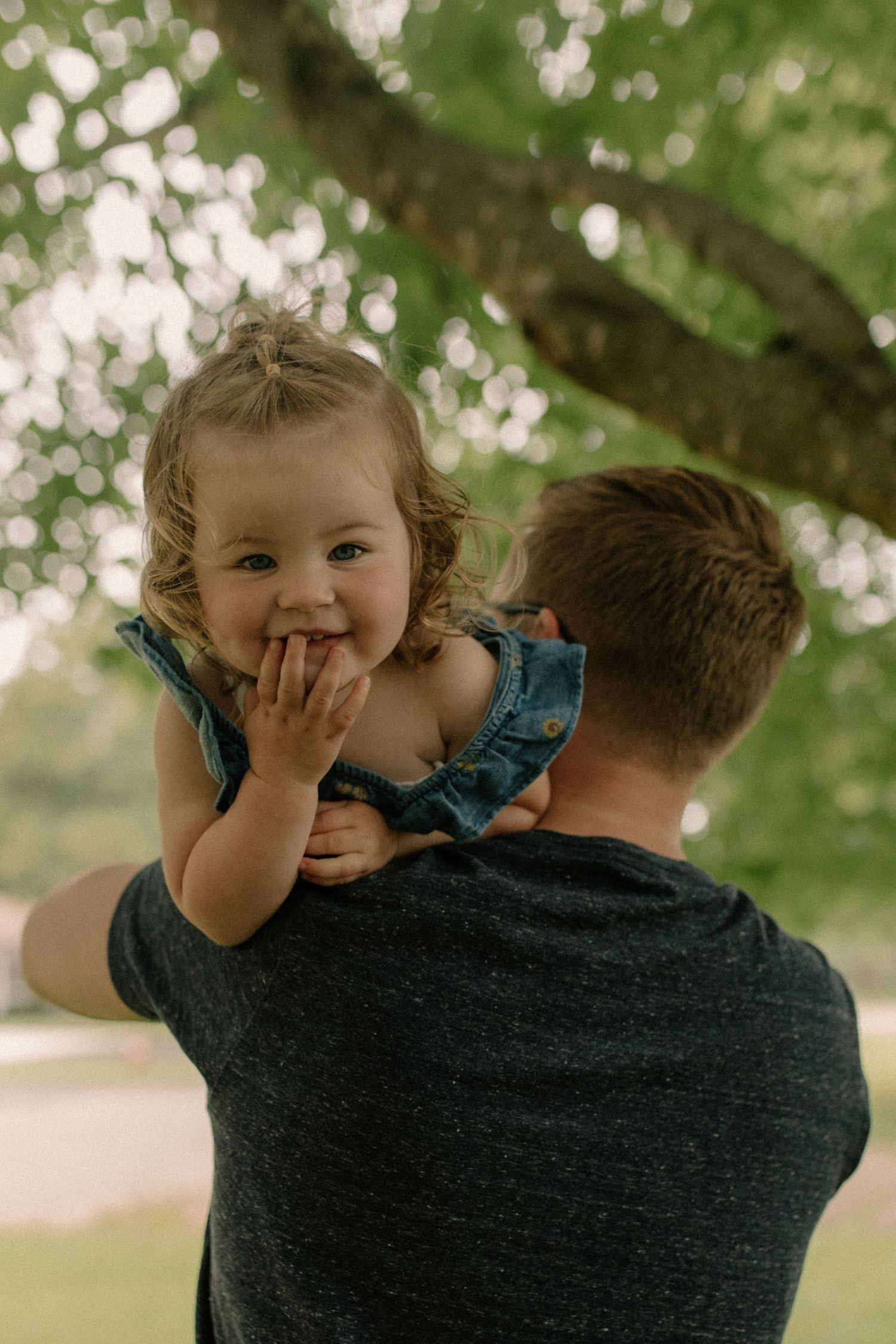 Sweet family moments captured under leafy green trees on a sunny day for outdoor family photos