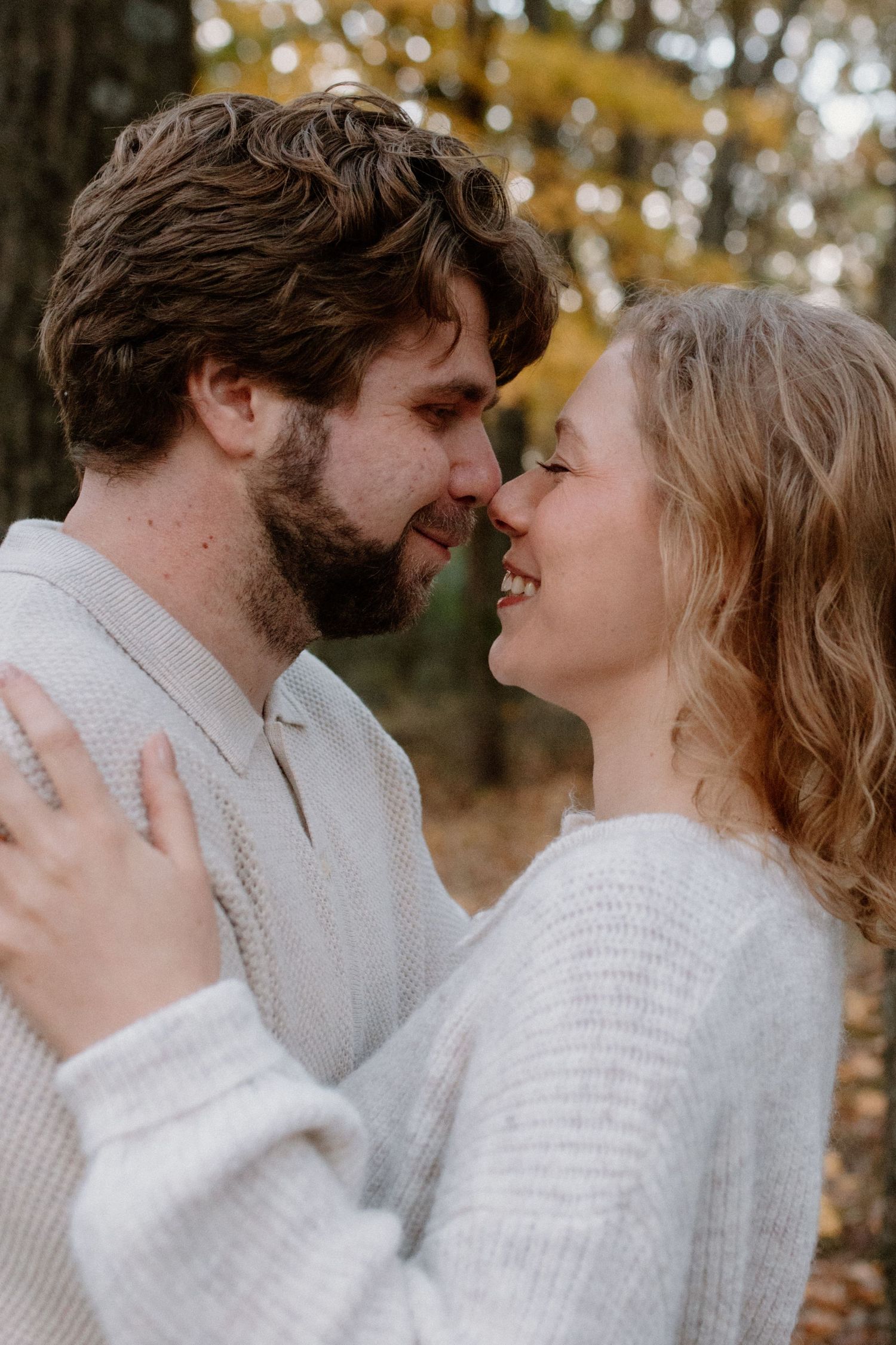 A close intimate moment between a couple wearing matching white sweaters in autumn setting engagement photos