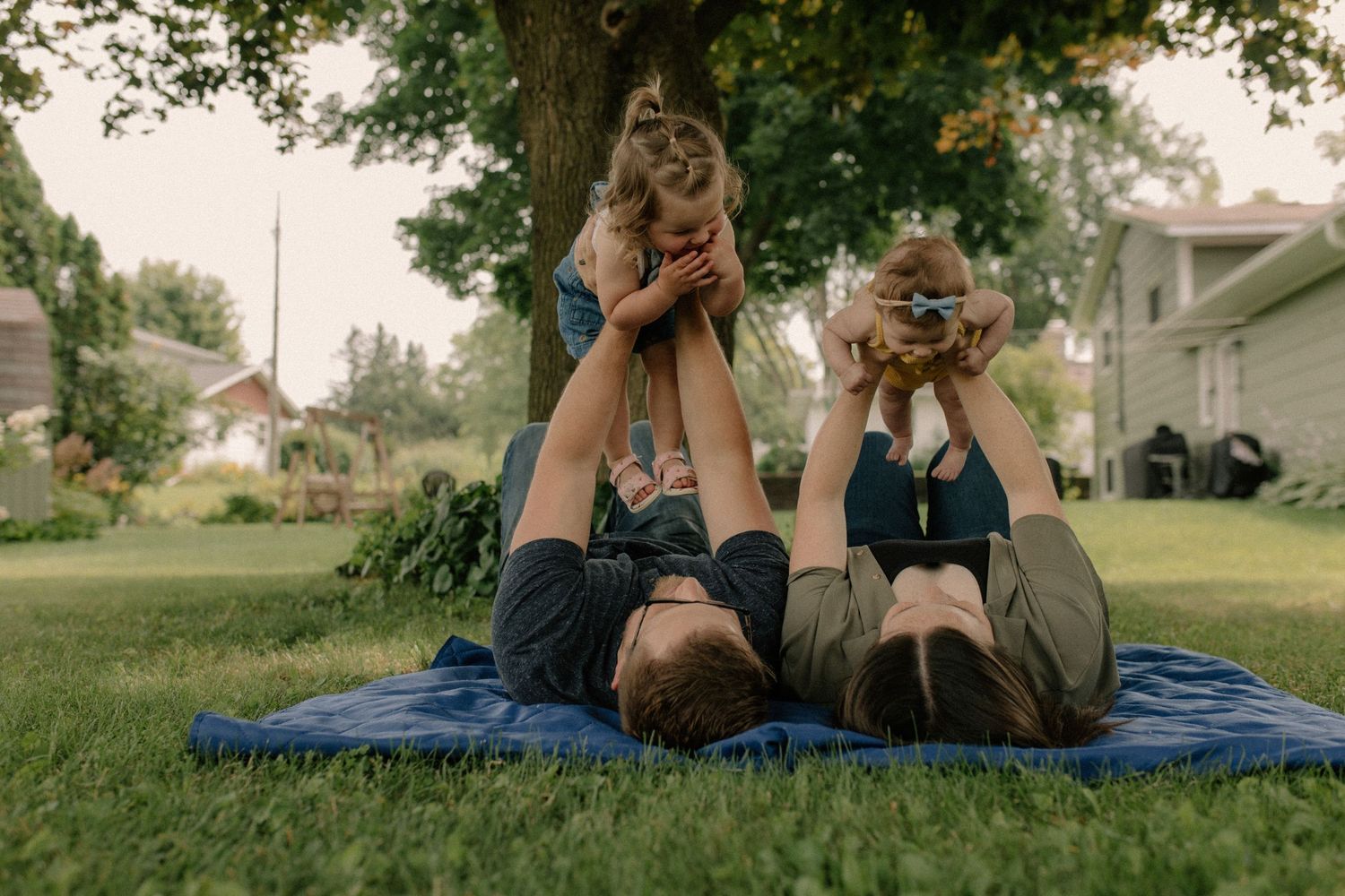Family lying on blue blanket in grassy field during golden hour for documentary-style family photos