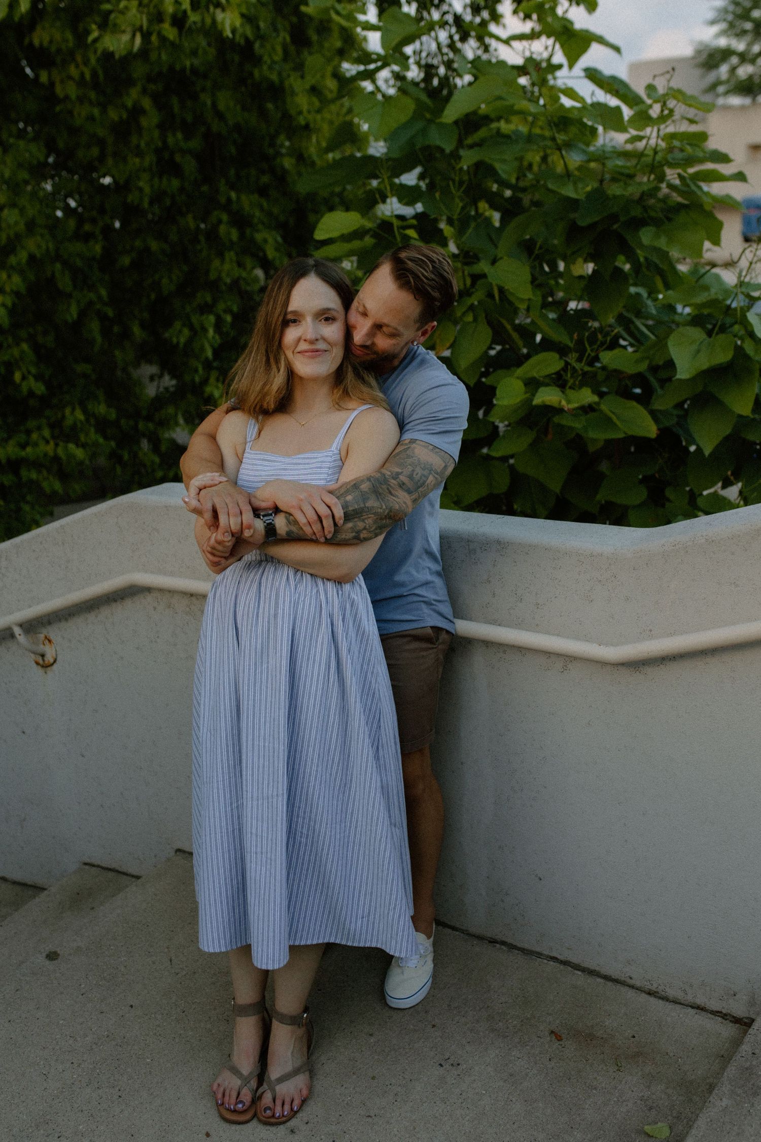 Couple sits together on white concrete steps surrounded by lush green foliage for Madison, WI couples photography session