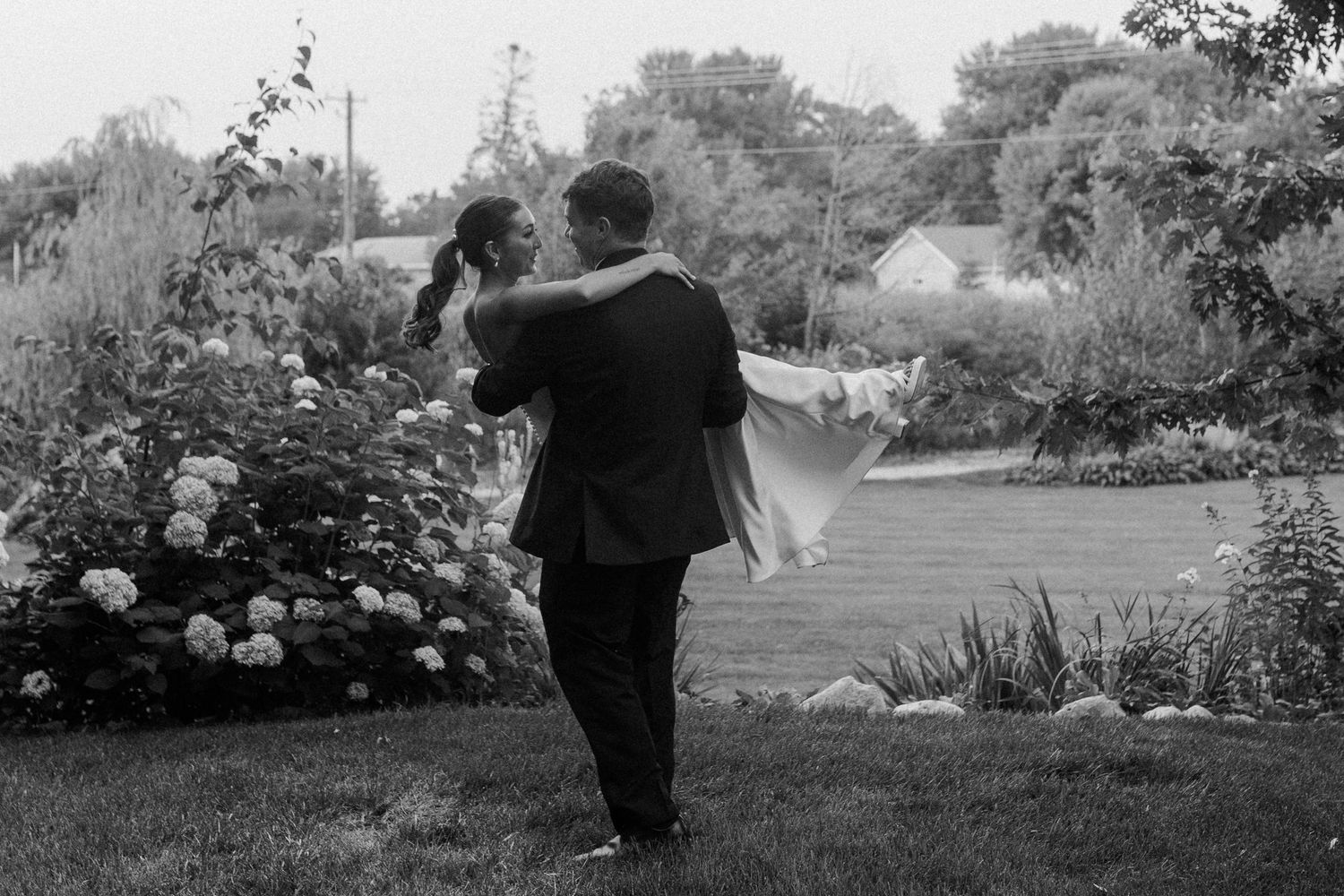 A couple walks through a lush garden path in black and white wedding attire at Wisconsin Gardens Wedding Center