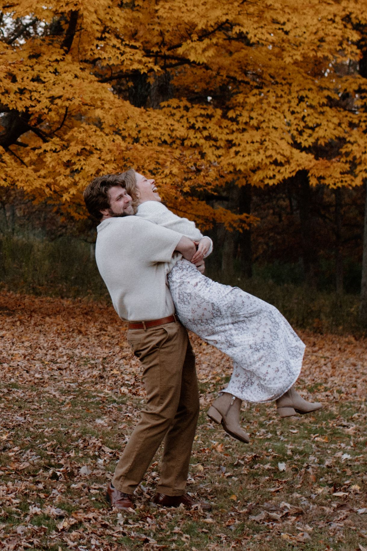 A romantic embrace captured against vibrant orange fall foliage in a wooded area during Wisconsin engagement session