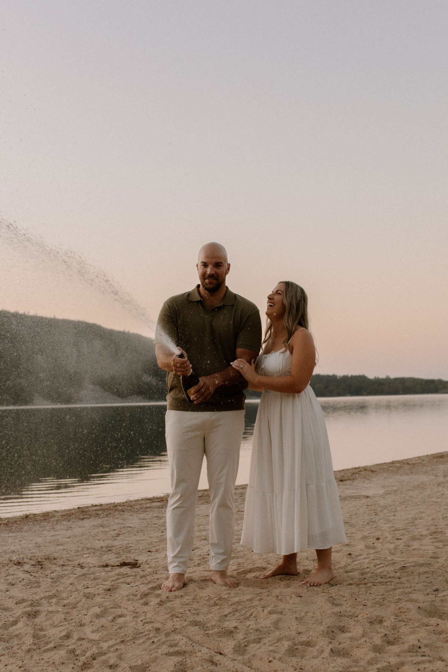 A couple celebrates with champagne on a sandy beach at sunset engagement session at Devil's Lake State Park