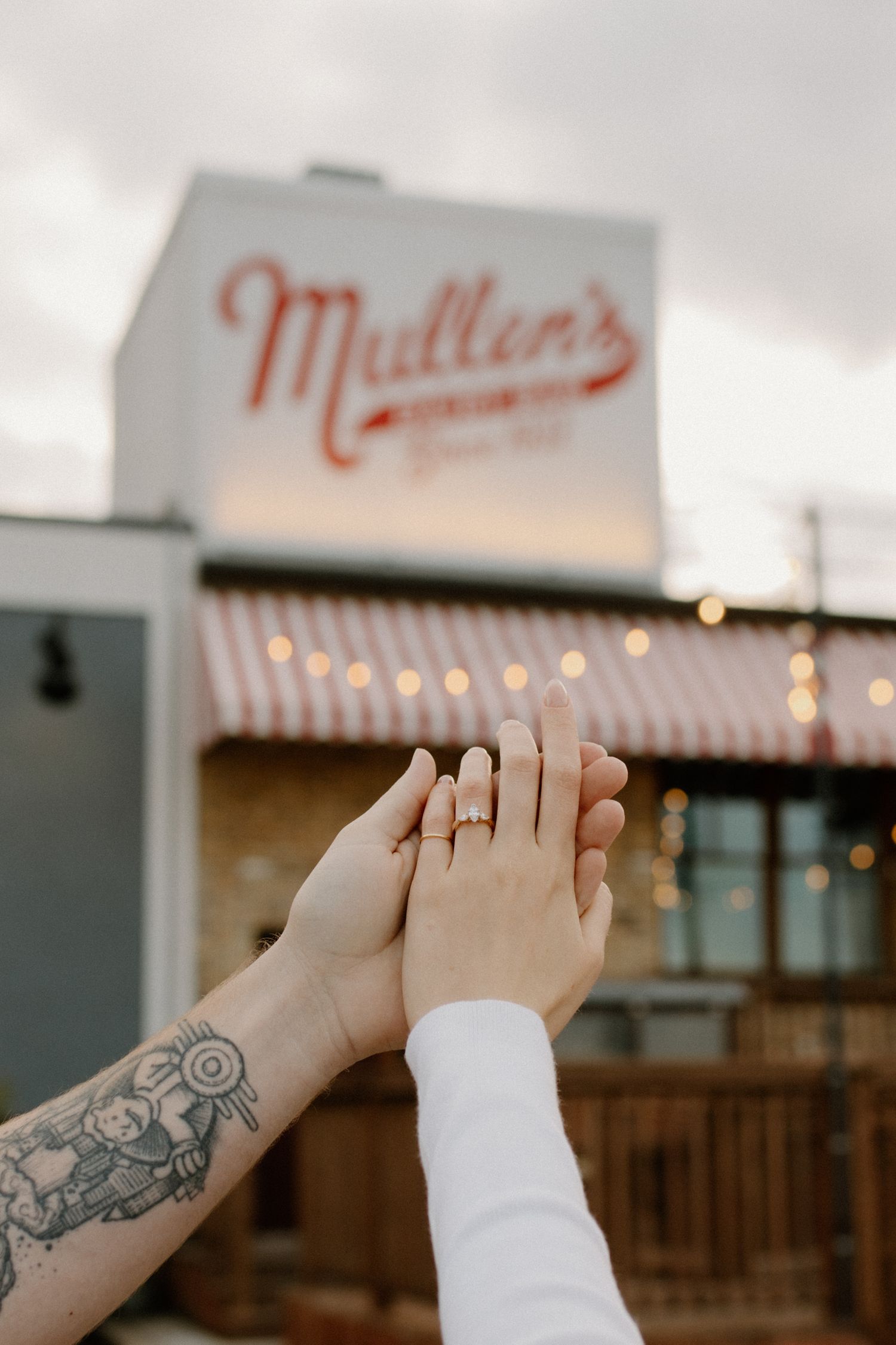 Engagement ring displayed on hands held in front of Mullen's restaurant sign in Oconomowoc engagement session