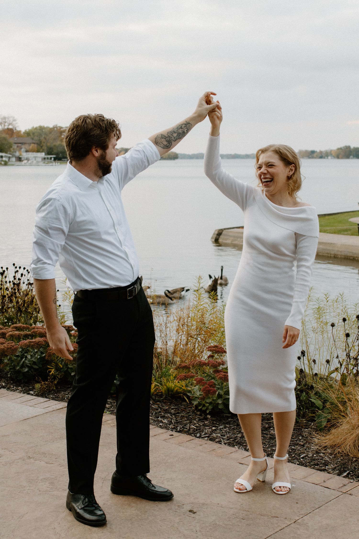 Couple dances and laughs together on a waterfront path during an overcast day in downtown Oconomowoc engagement session
