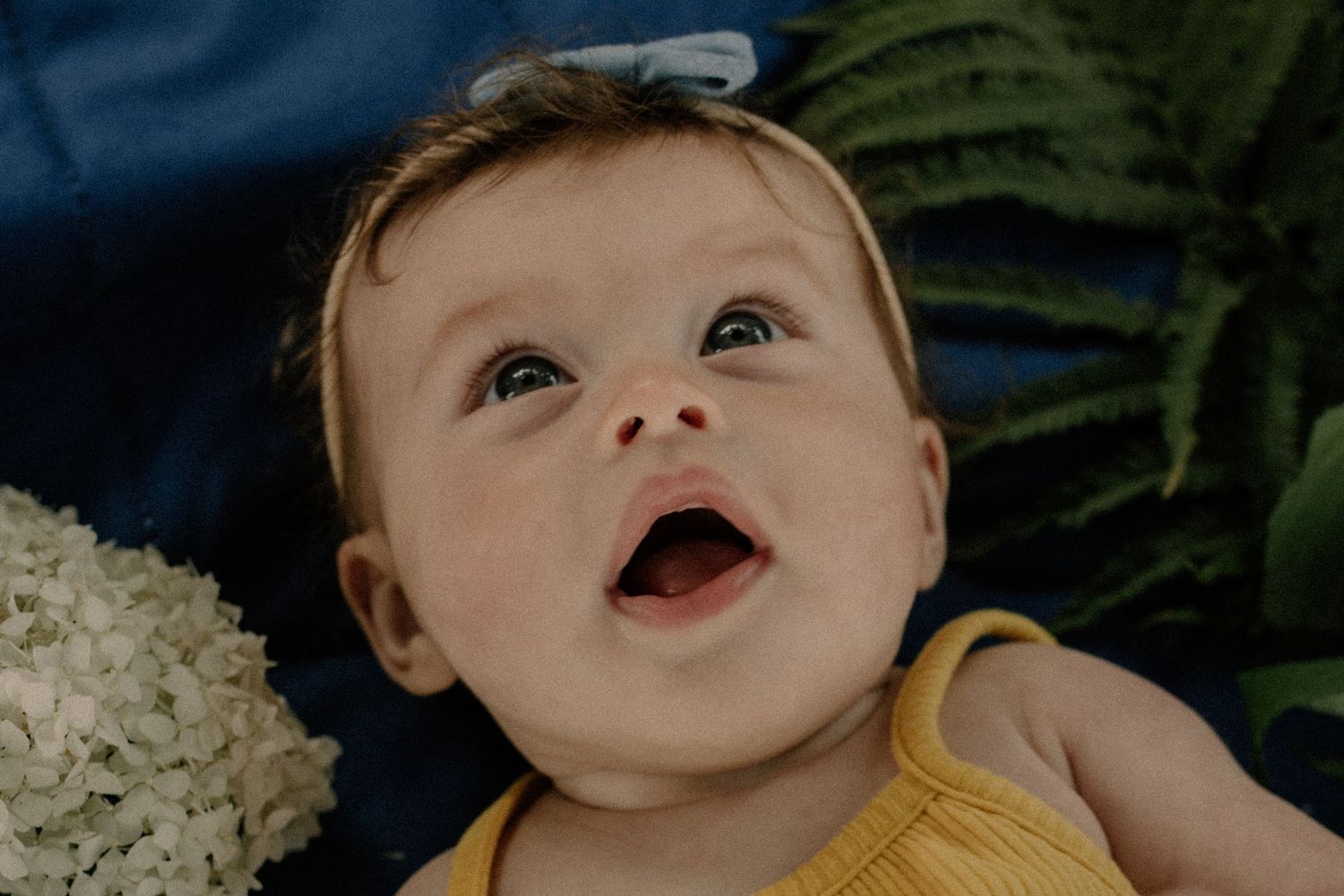 A baby posed for family photos wearing a yellow top smiles brightly while lying down