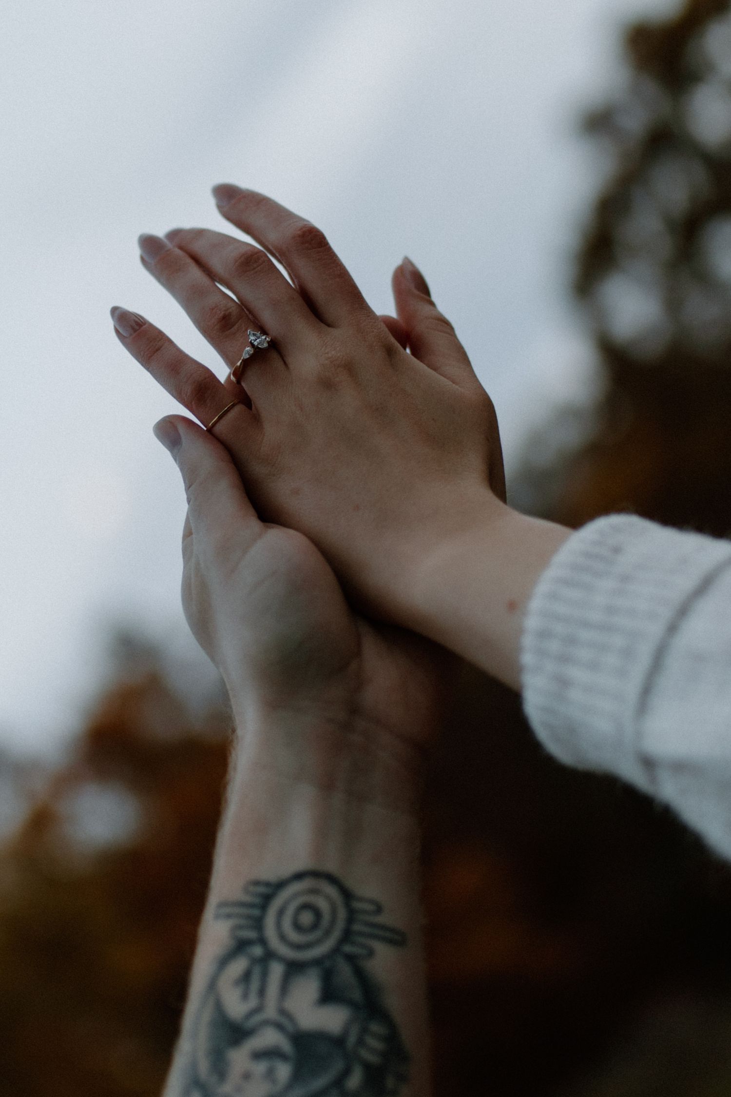 Close-up of arms with tattoos reaching towards each other against a moody sky