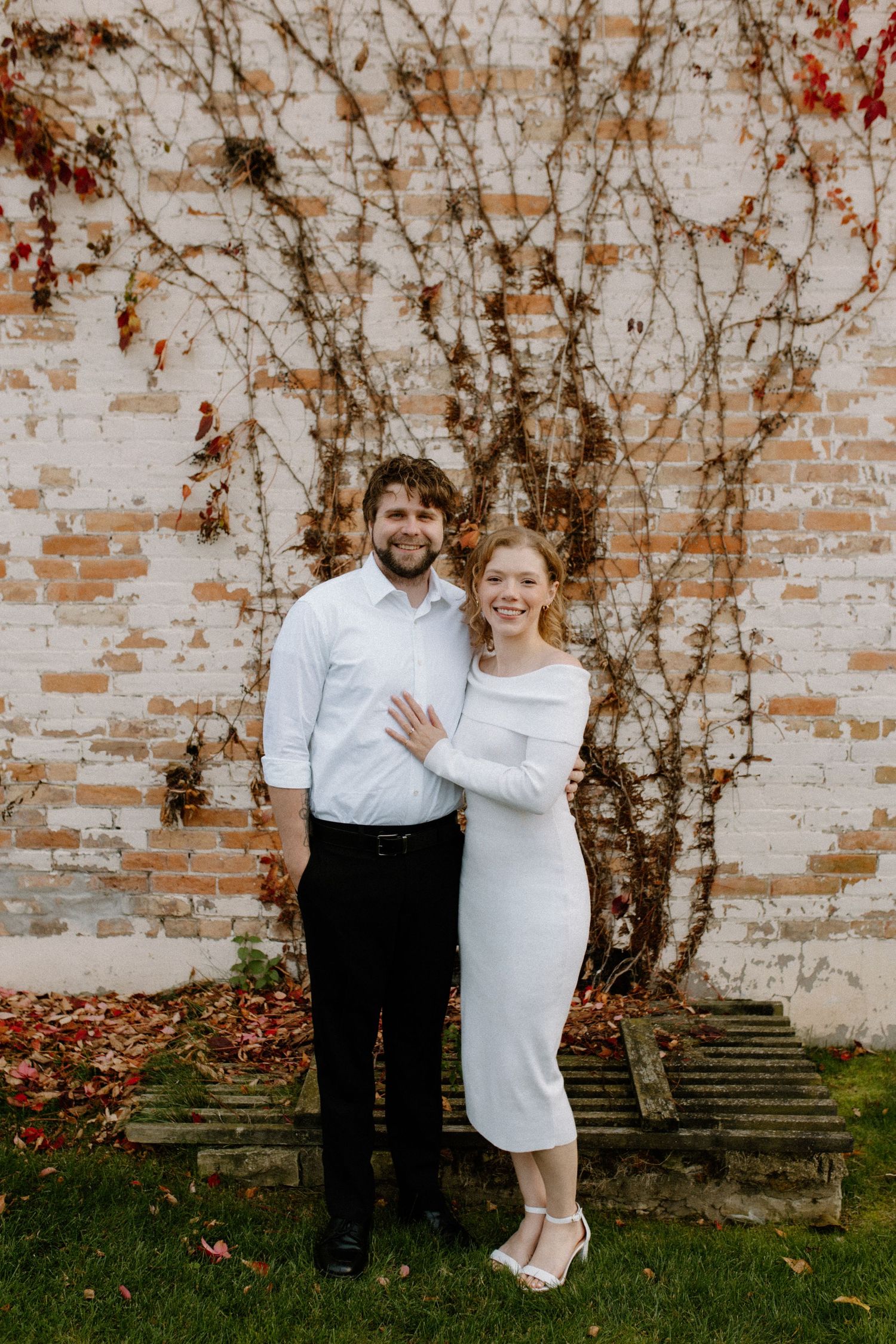 Romantic couple shares playful moments against an ivy-covered brick wall backdrop in downtown Oconomowoc engagement session