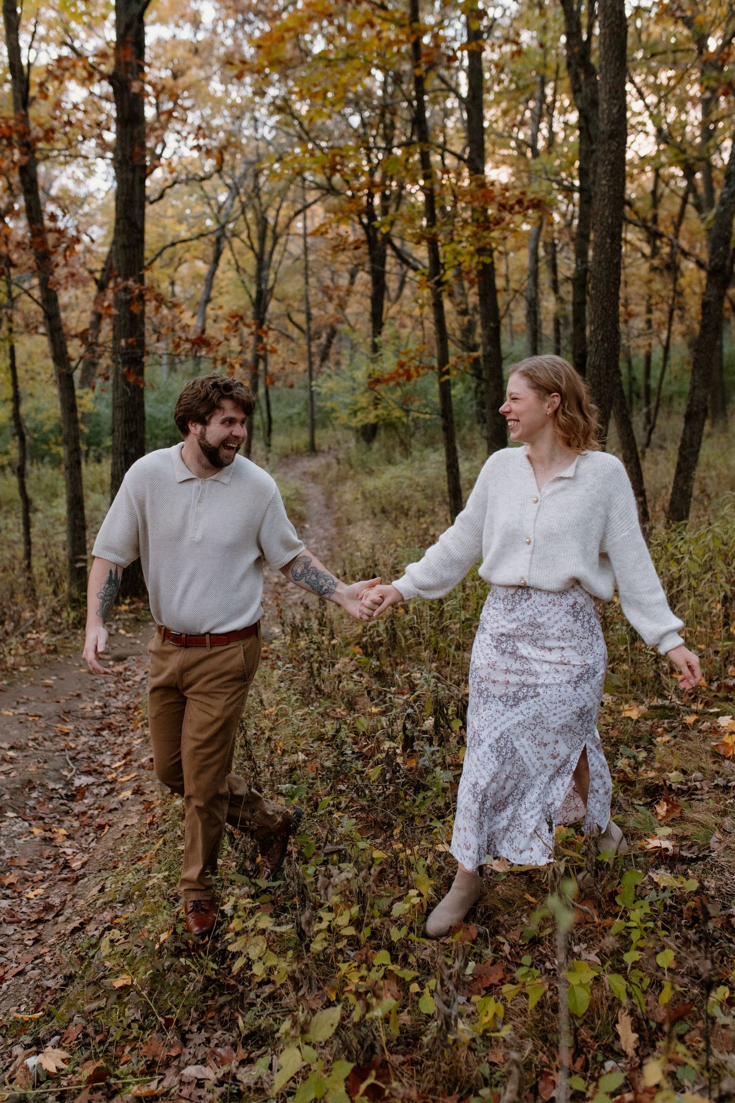 A couple playfully dances through fallen leaves on a wooded trail at Lapham Peak engagement session