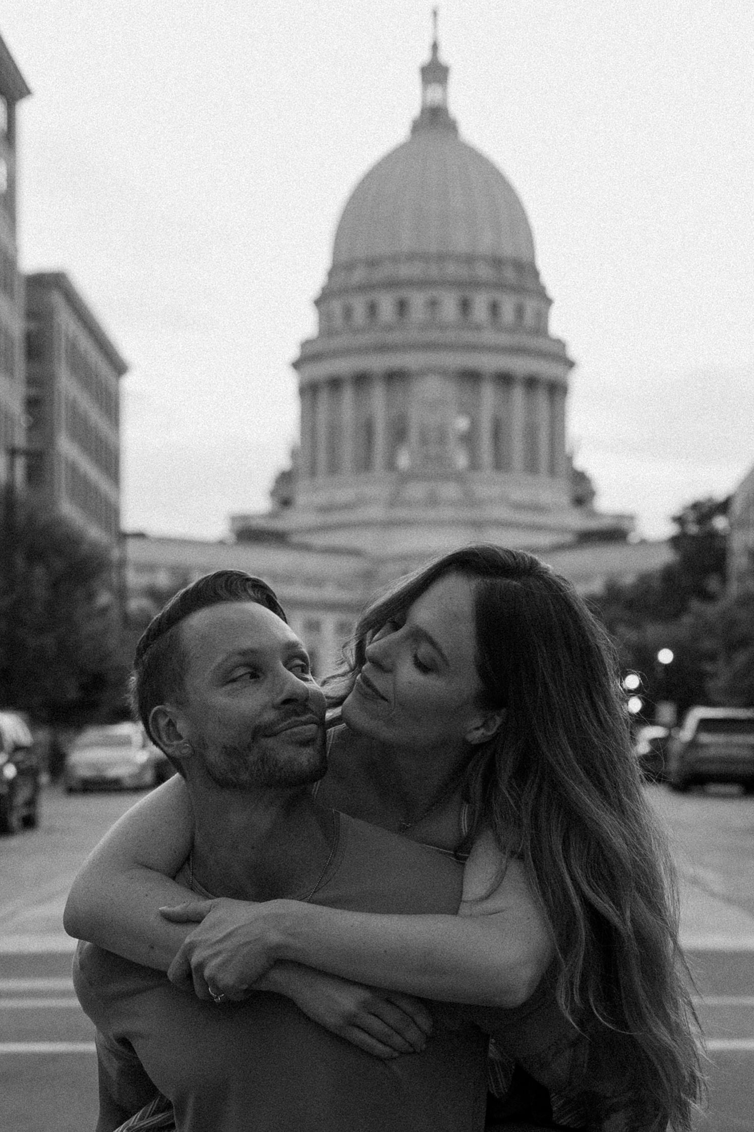 Black and white photo of couple embracing with Wisconsin State Capitol dome in background for couples photography session