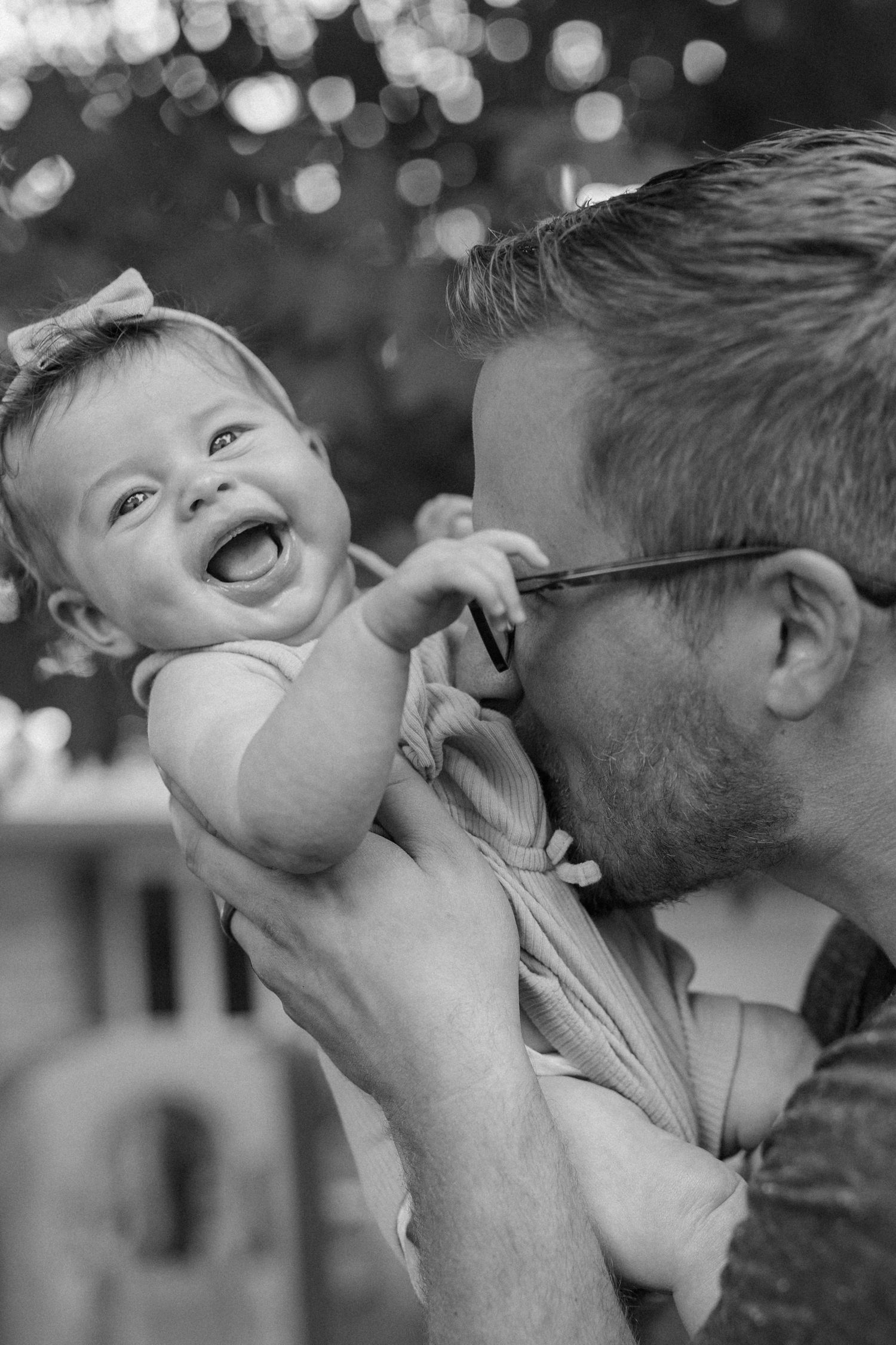 Black and white photo of baby being lifted up with natural bokeh lighting for outdoor family photos