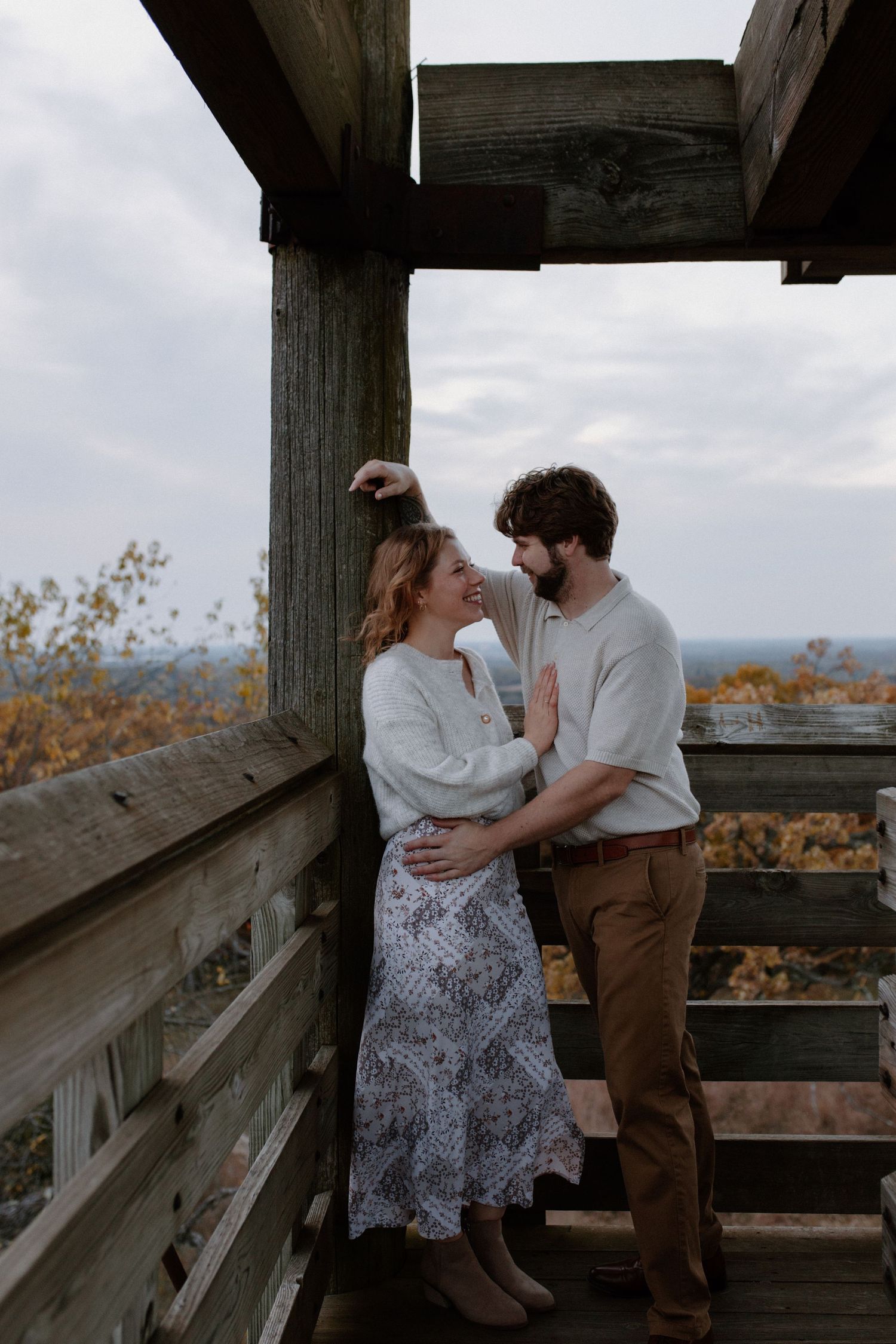 A romantic moment shared on an elevated wooden deck with fall foliage in the background at Lapham Peak engagement session