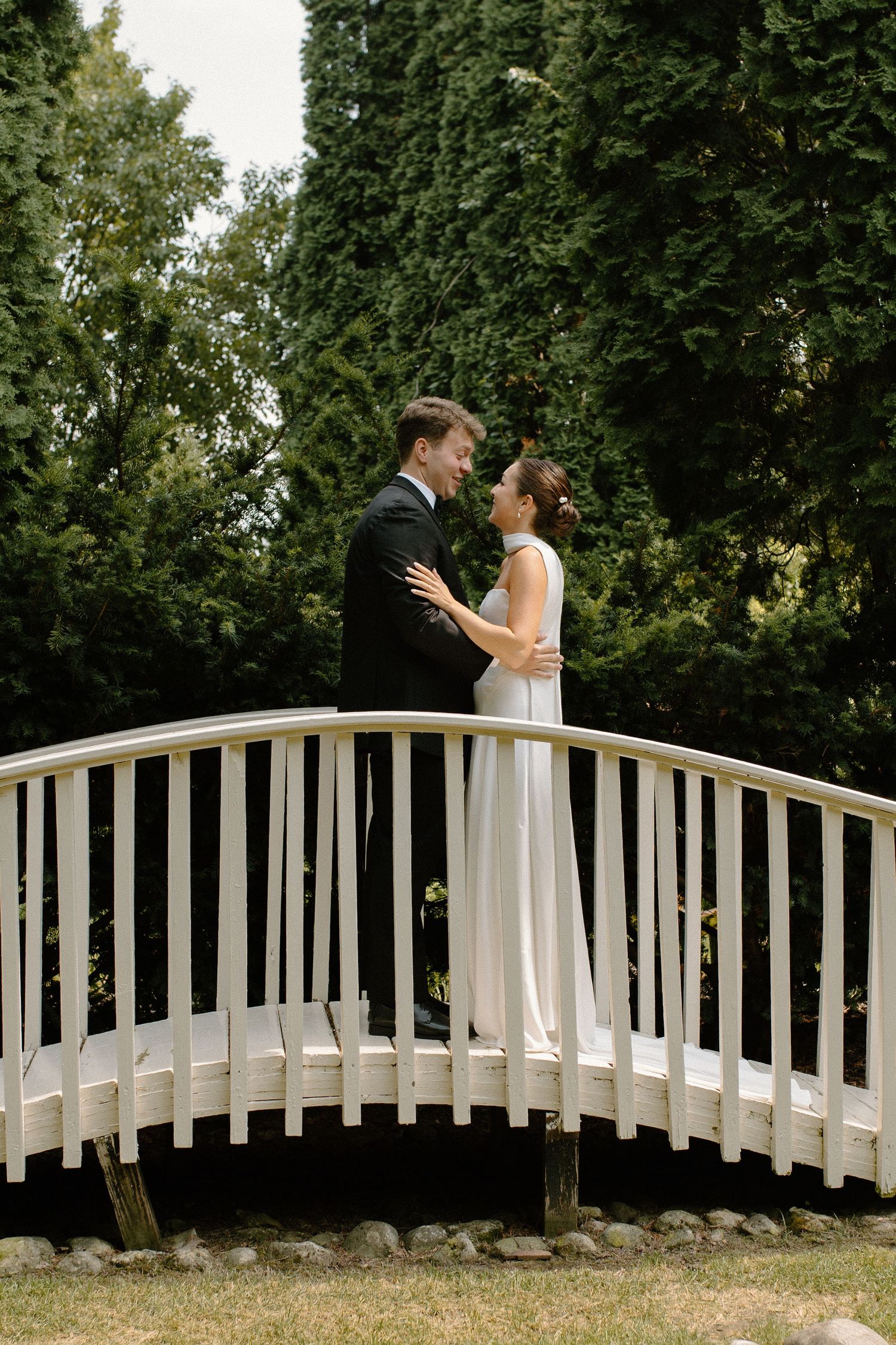 Bride and groom pose on bridge in greenery during Wisconsin garden center wedding