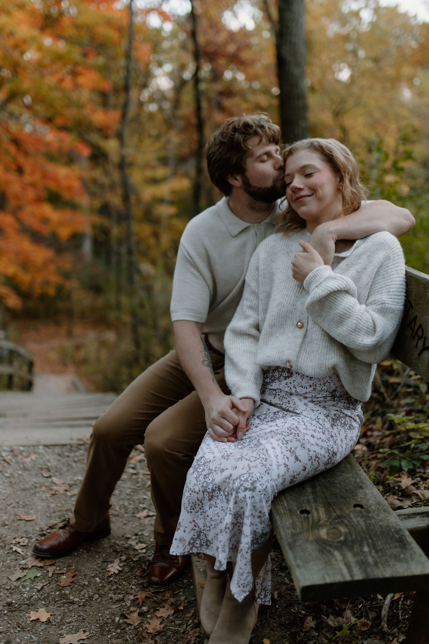 A romantic moment shared on a wooden bench surrounded by autumn trees at Lapham Peak engagement session