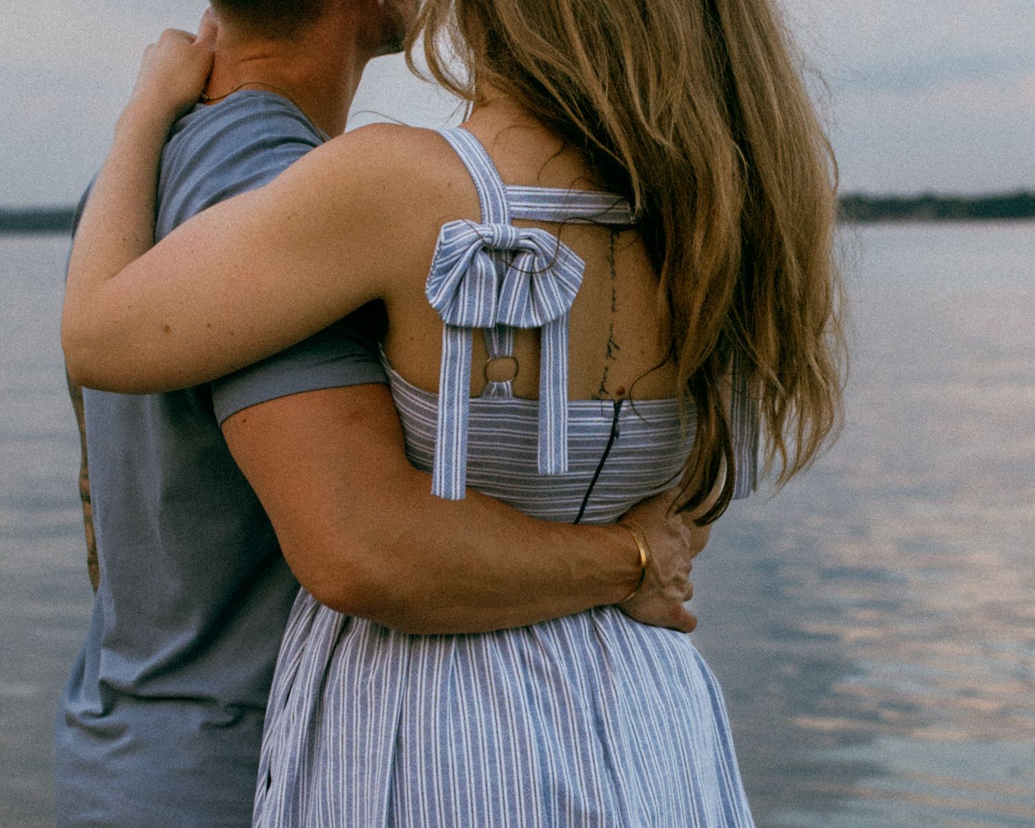 Romantic couple embraces at sunset by Lake Mendota in Madison, WI with soft lighting and reflective water for couples photography session
