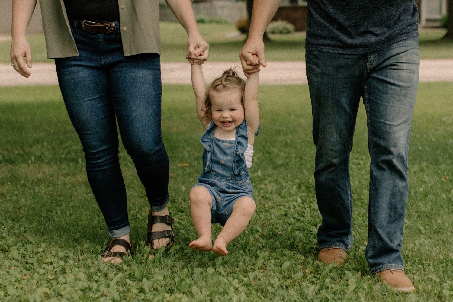 Family members walking together on green grass with child between them for outdoor family photos