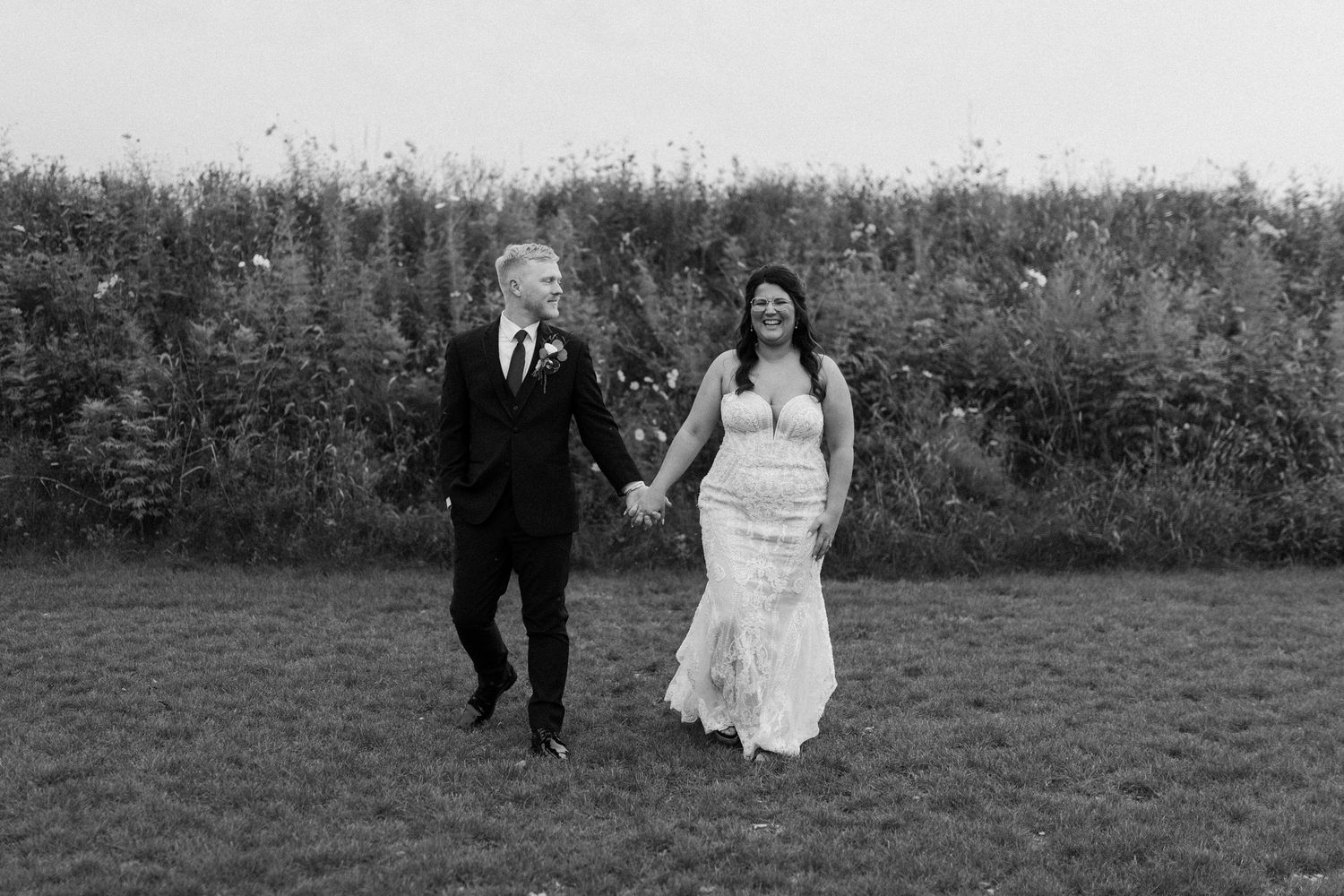 A couple walks hand in hand across a grassy field in their wedding attire in Oconomowoc wedding at The Valerie