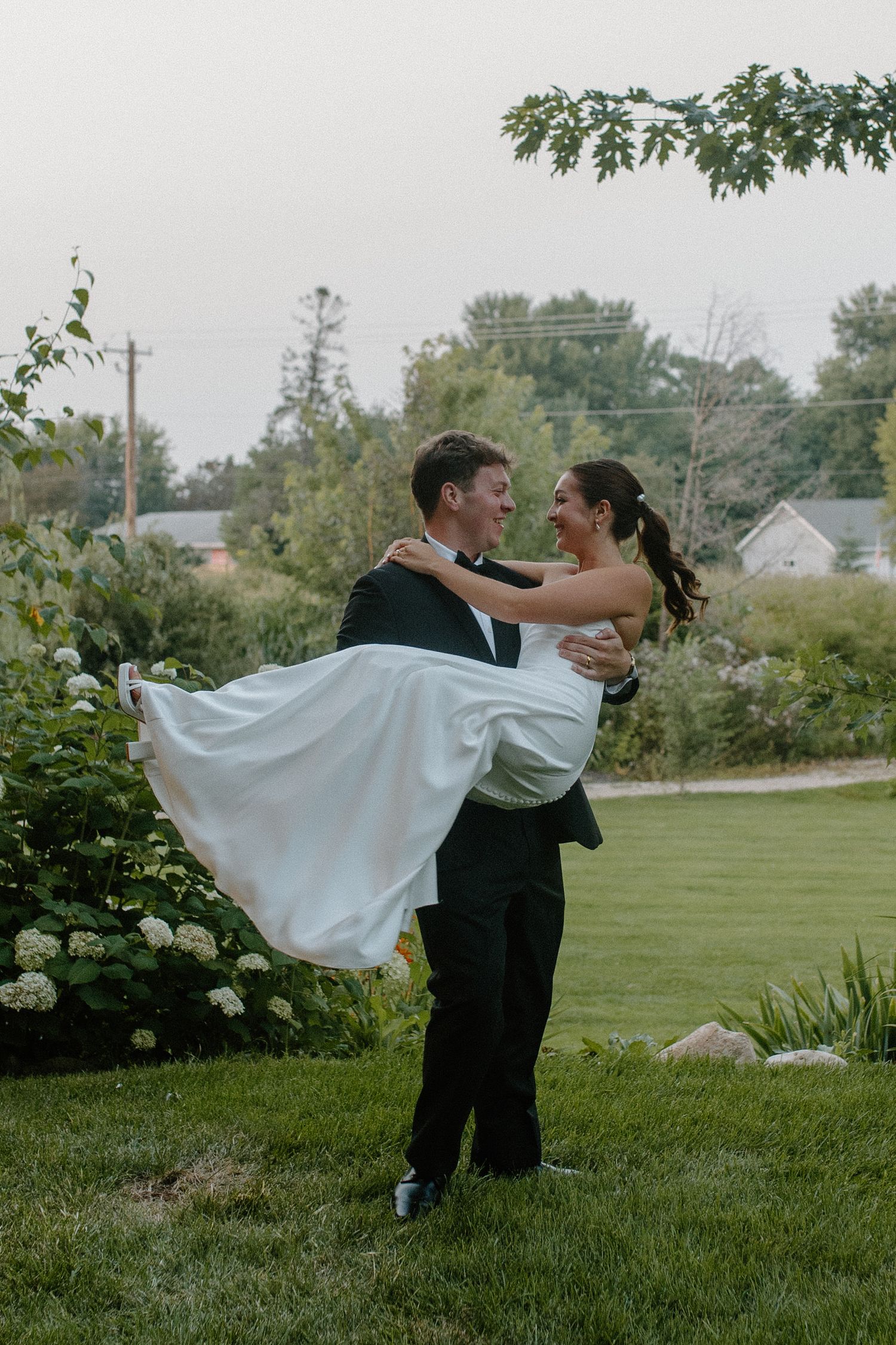 Groom with bride in his arms spins romantically on green lawn at Gardens Wedding Center in Wisconsin garden wedding
