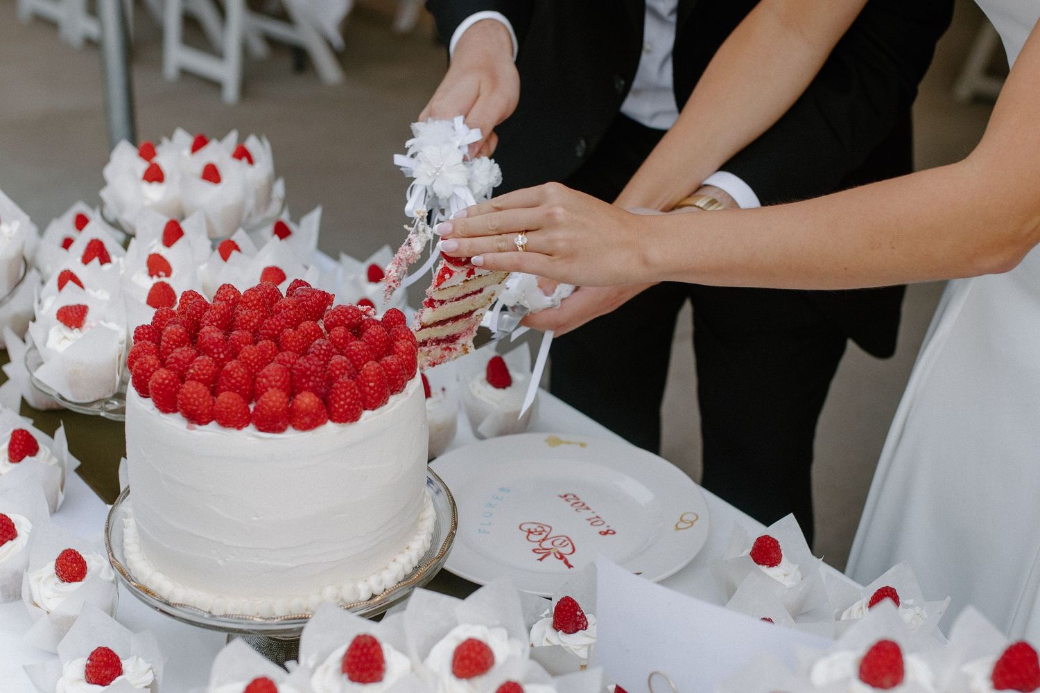 Bride and groom cutting a white wedding cake topped with fresh raspberries, surrounded by matching raspberry desserts.