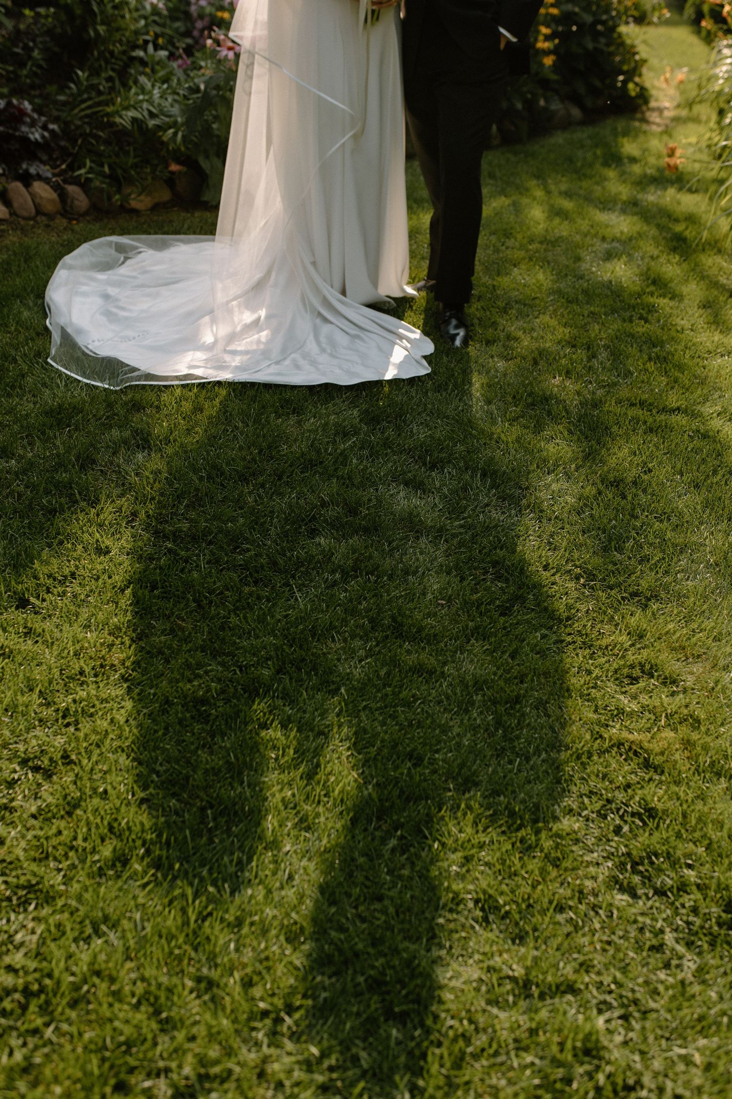 Long shadows cast on green grass by wedding party figures in afternoon sunlight at Wisconsin gardens center wedding venue