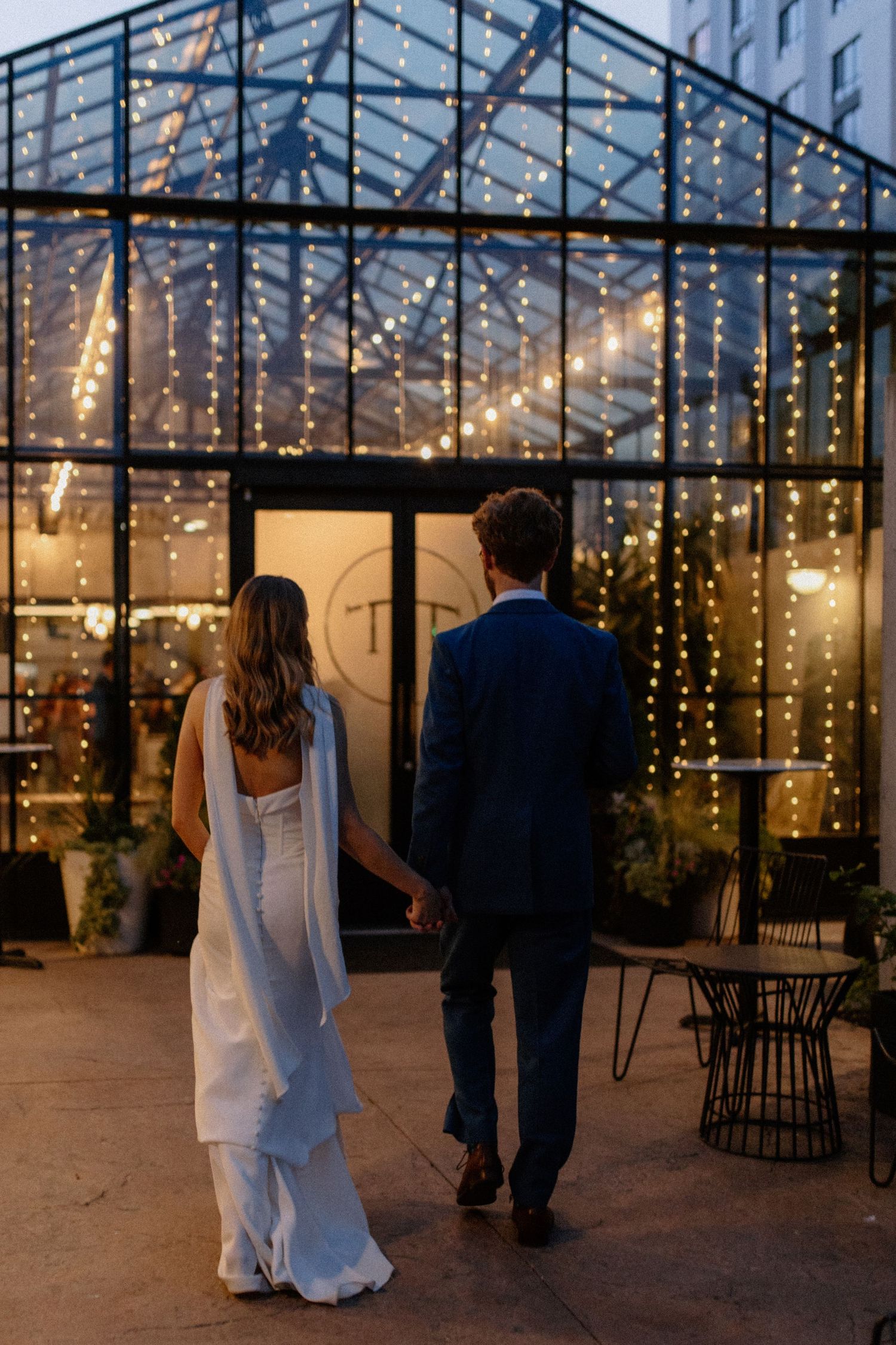 A couple walks near The Tinsmith wedding venue decorated with twinkling string lights at dusk