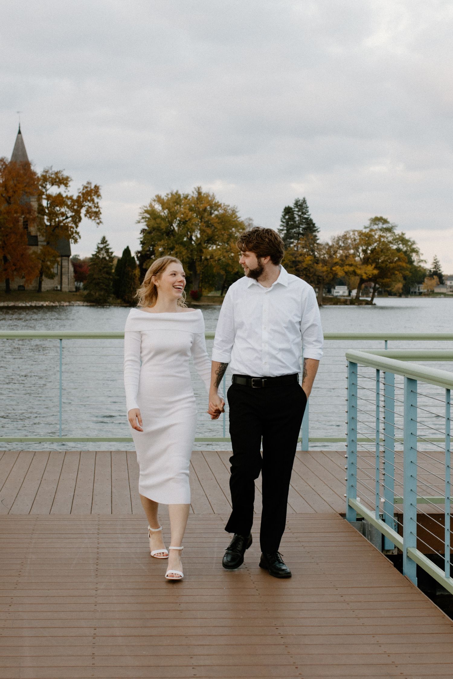 Couple takes a romantic stroll on a wooden pier in downtown Oconomowoc boardwalk engagement session