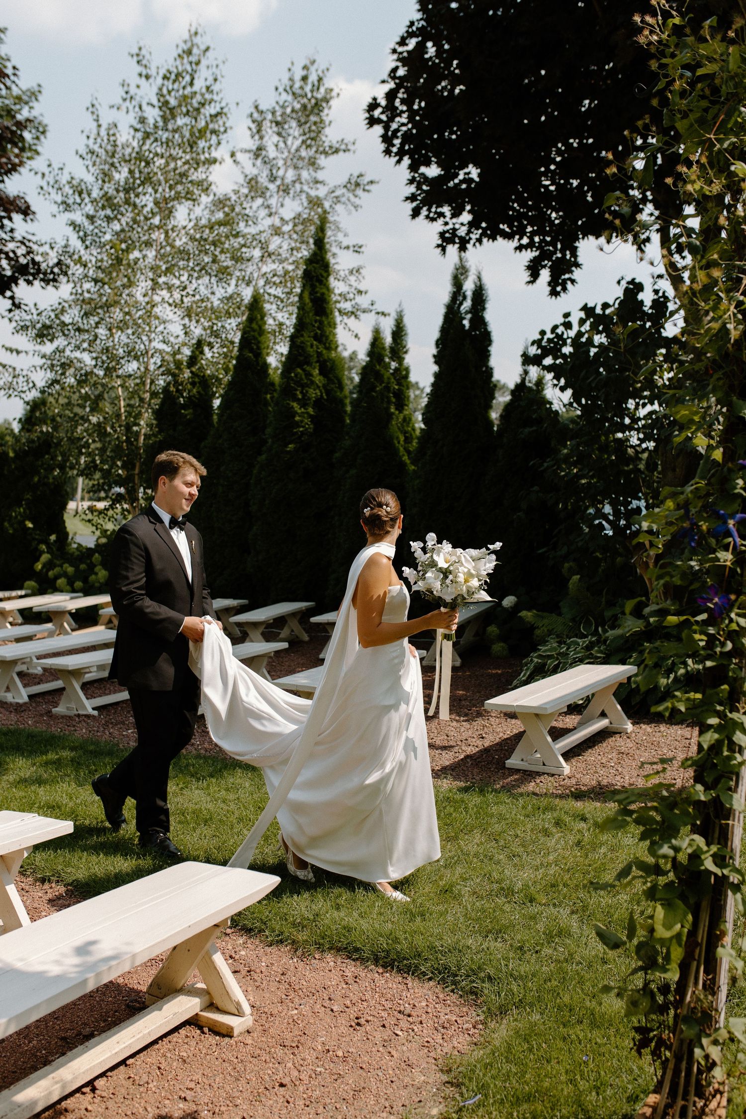 Wedding couple walks through garden with flowing white dress train and summer flowers at Wisconsin Gardens Wedding Center