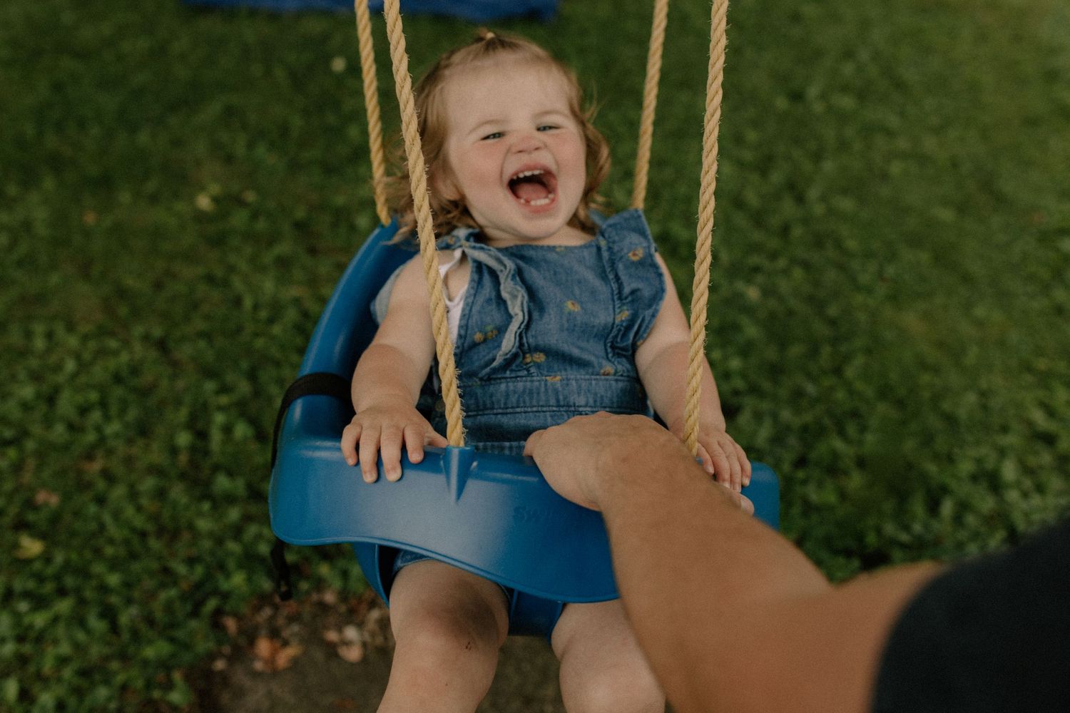 A child swinging joyfully on a wooden swing in a backyard setting for documentary-style family photos