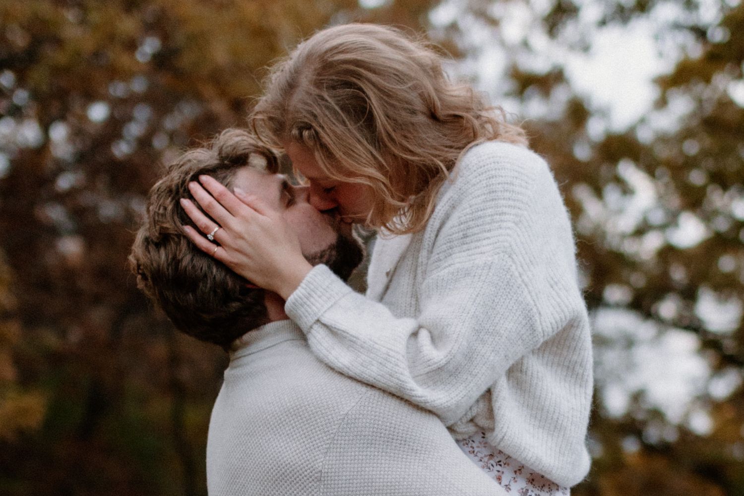 Man and woman embracing at outdoor engagement session against fall foliage background