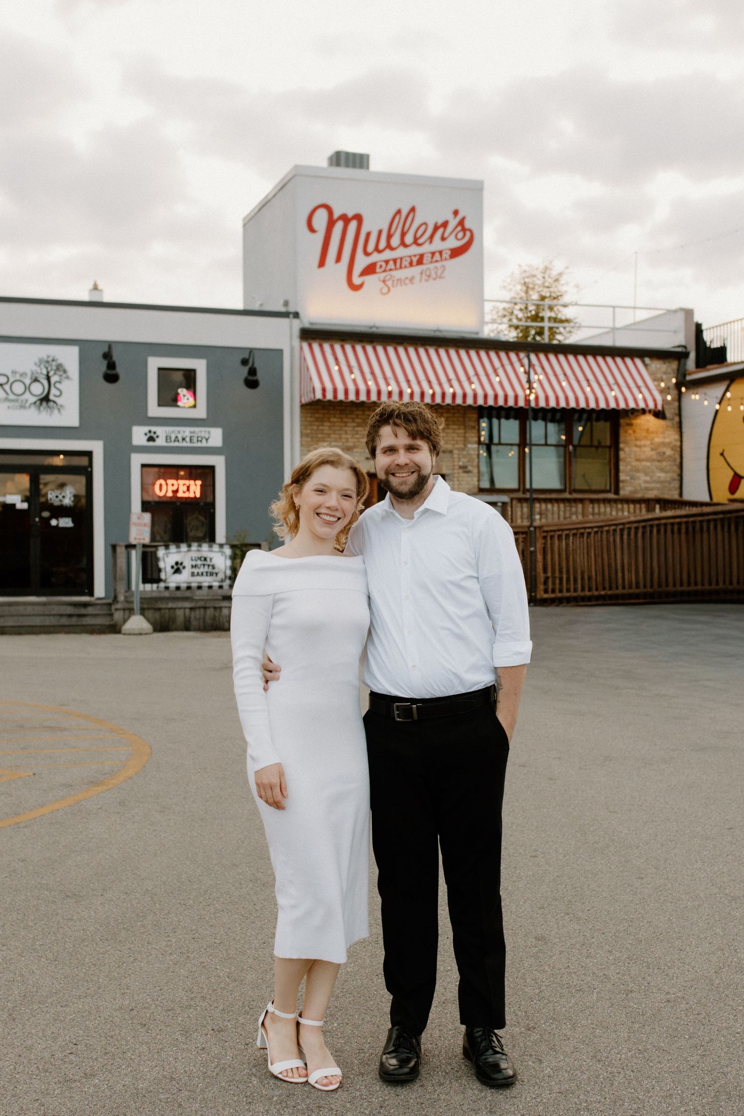 A couple poses together in front of Mullen's restaurant with a retro striped awning during Oconomowoc engagement session