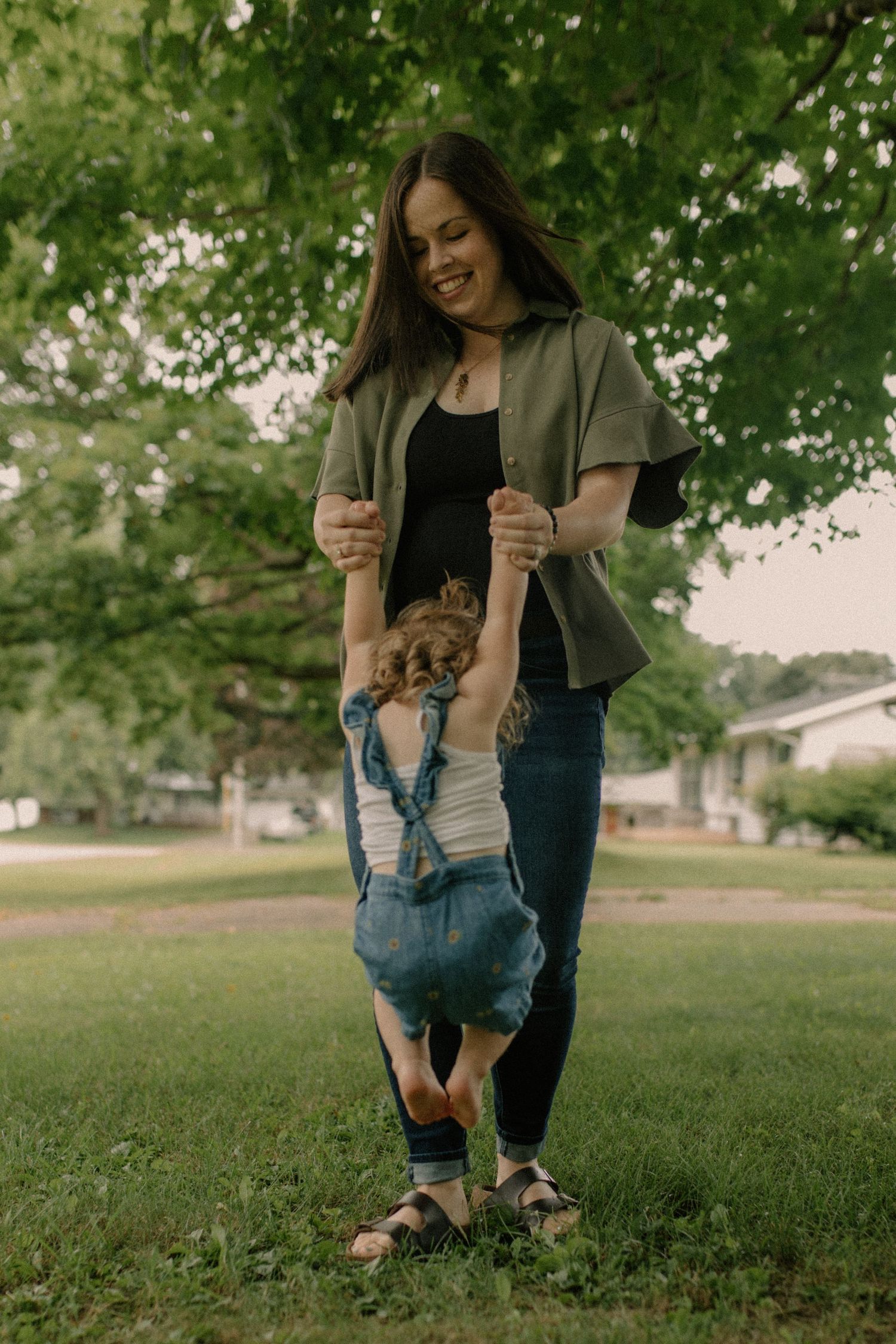 Family playing and laughing together on a grassy lawn under trees for outdoor family photos