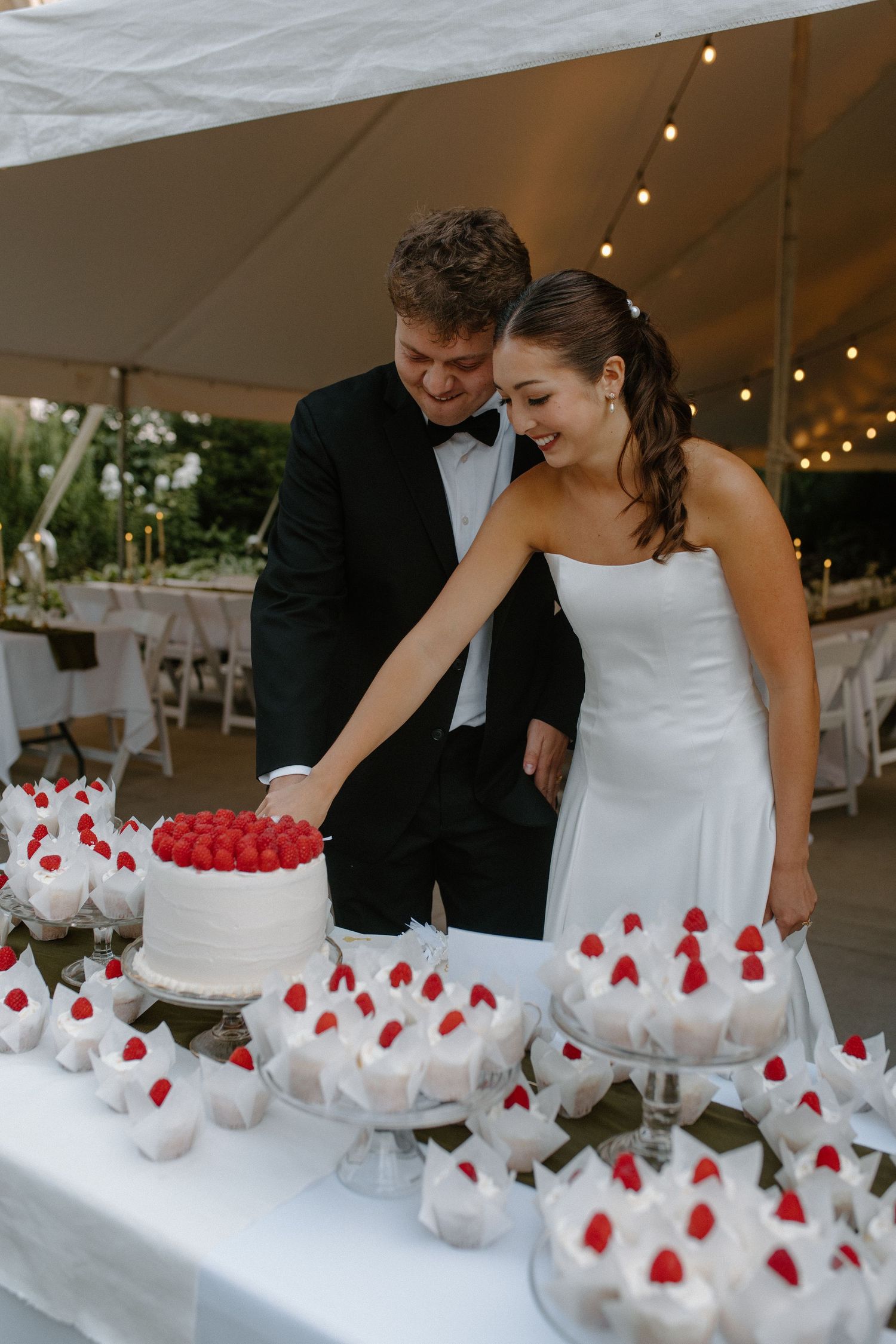 Wedding couple cutting cupcakes decorated with red berries under a white tent at Gardens Wedding Center in Wisconsin