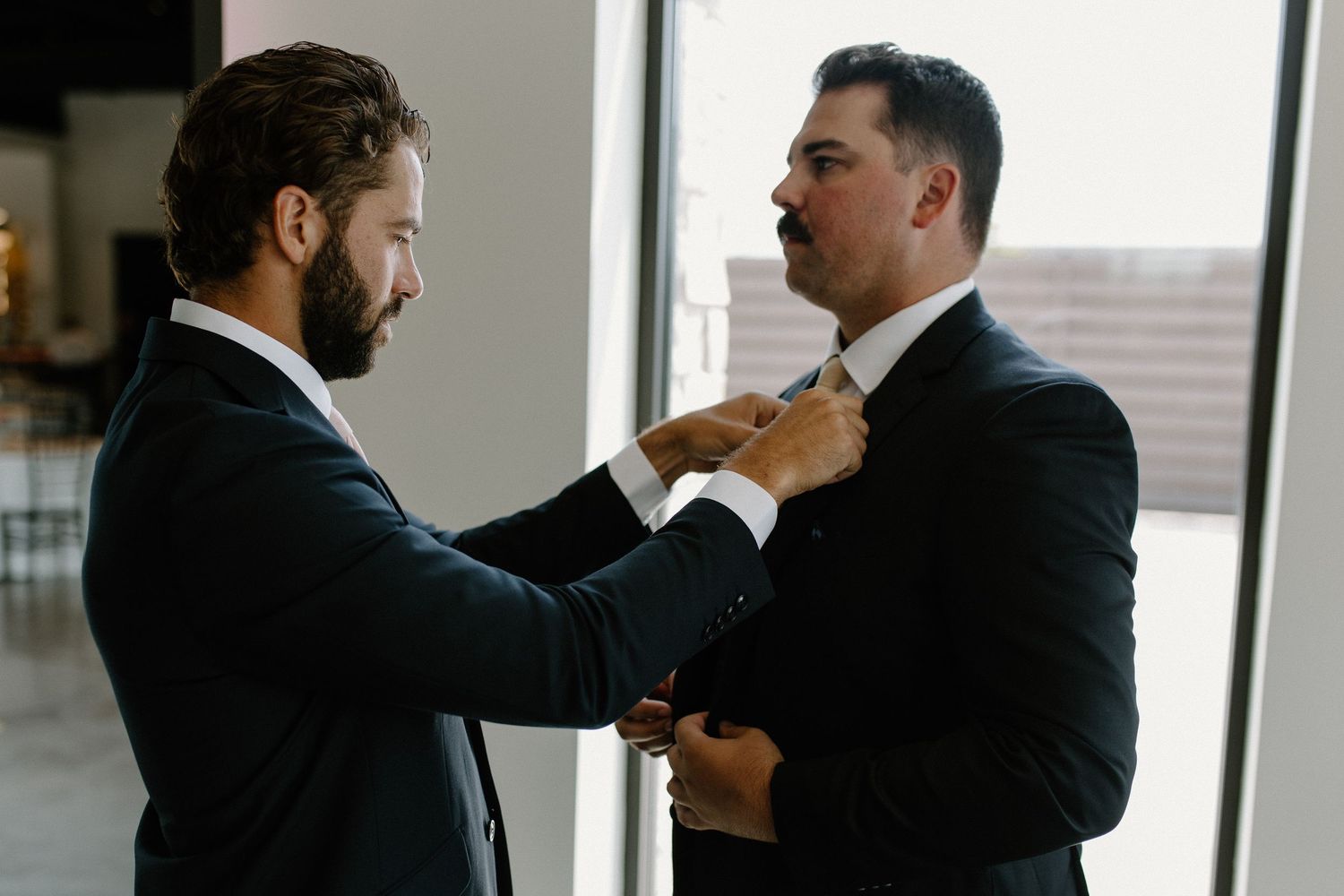 Groomsmen adjusting ties and getting ready by window at The Valerie wedding venue