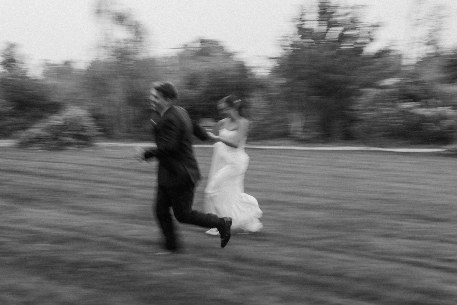 Motion blur captures running bride and groom in black and white at Gardens Wedding Center wedding