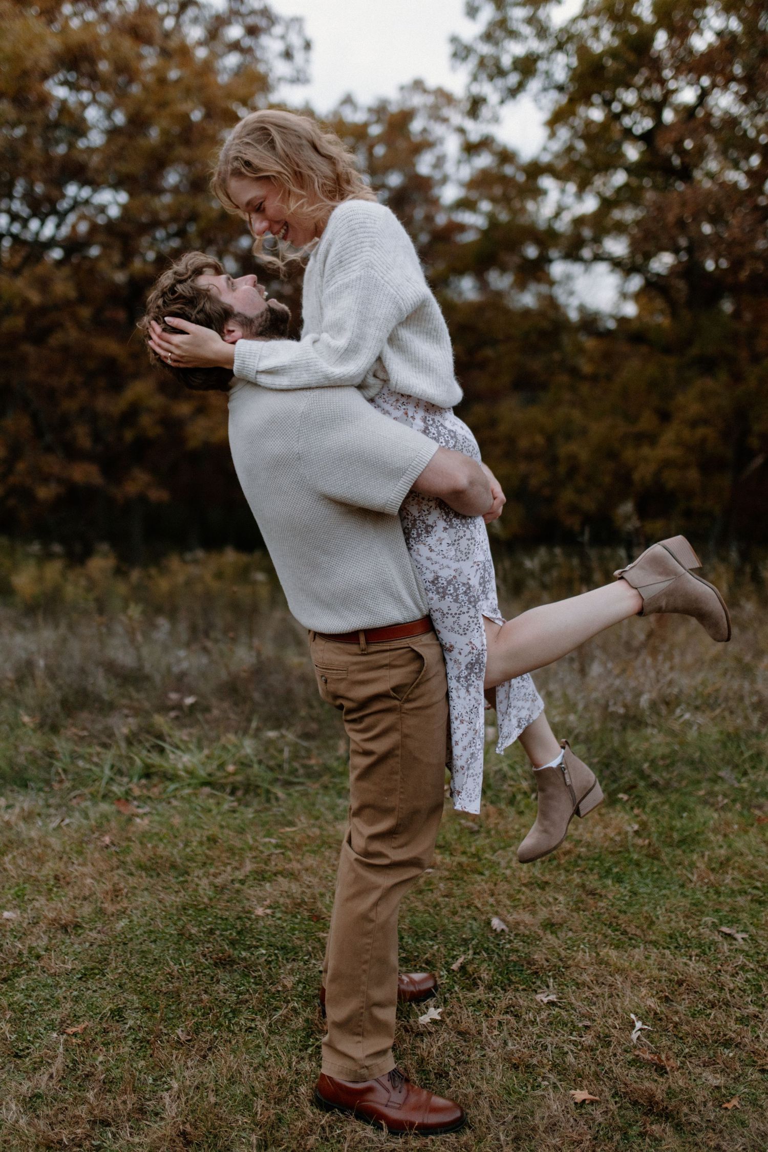 A couple dances playfully in a field with autumn trees in the background at Lapham Peak engagement session