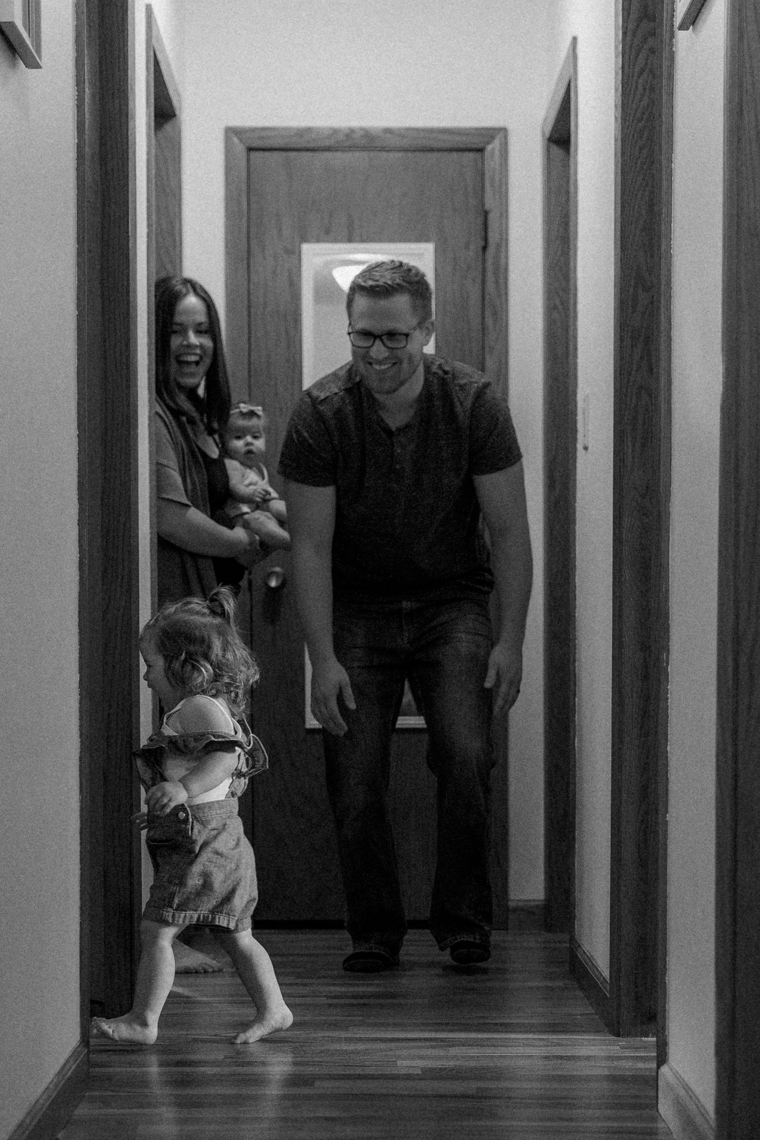 Playful black and white in-home family photo session with toddlers running and parents chasing