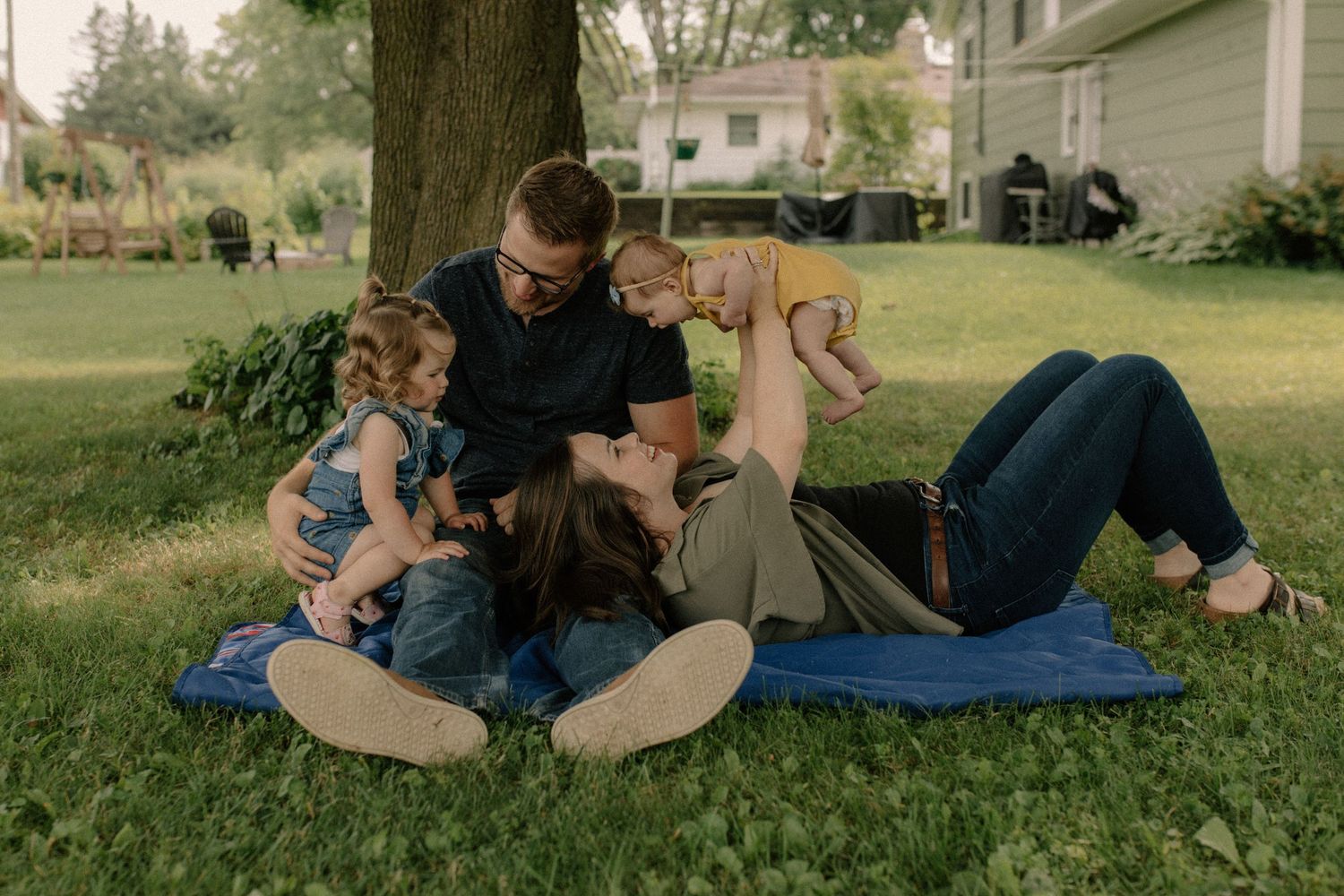 Family relaxing together on a blue blanket in a grassy outdoor setting for documentary-style family photos