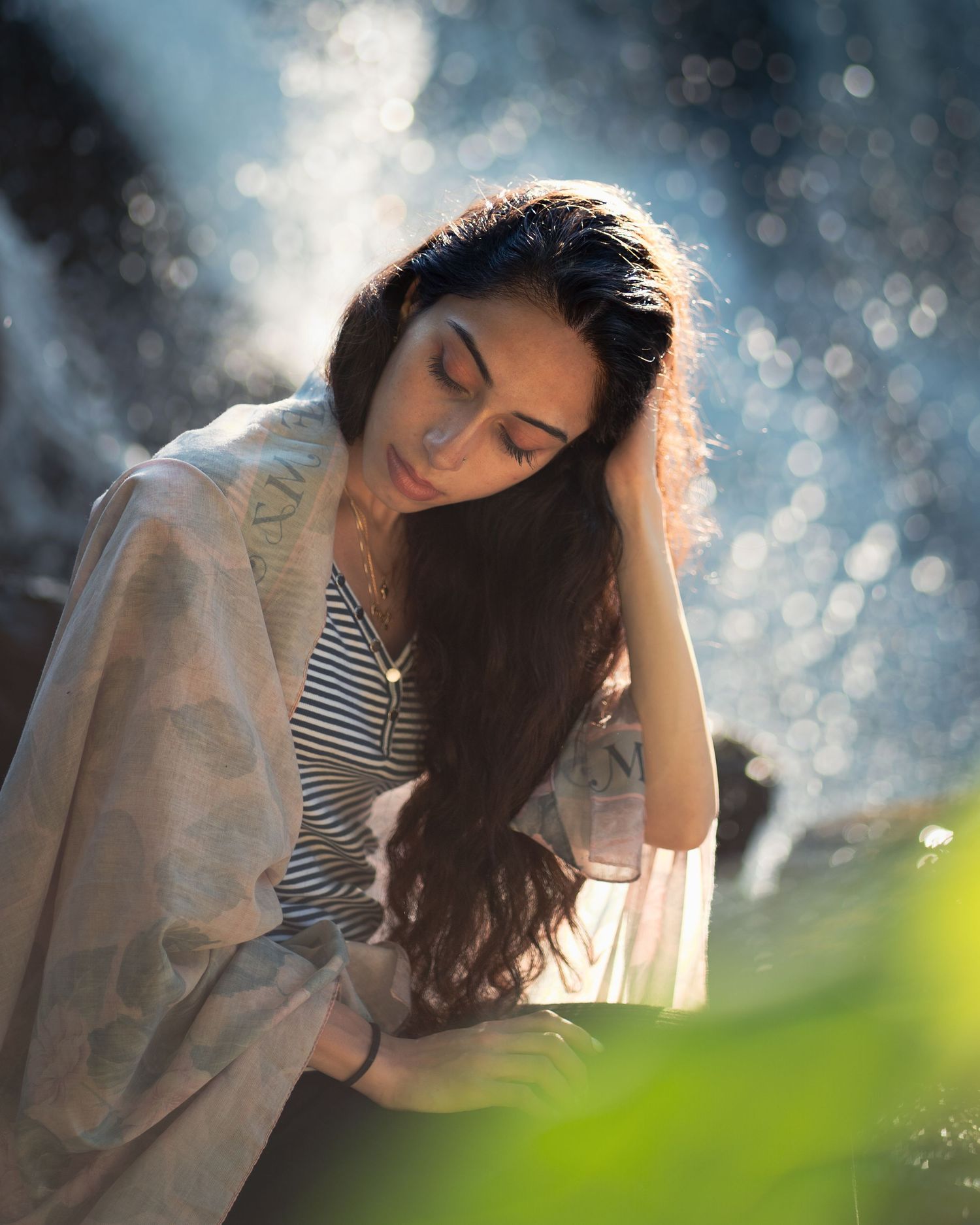 A person in striped clothing sits with soft bokeh light effects and natural sunlight in the background.