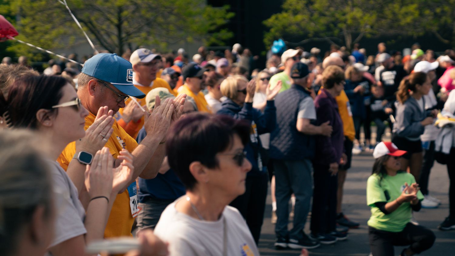 Large crowd gathered outdoors during daytime event with trees in background.