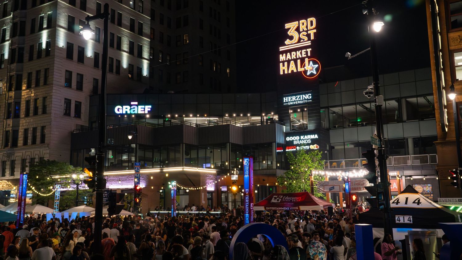 Nighttime cityscape with illuminated signs and crowded street festival.