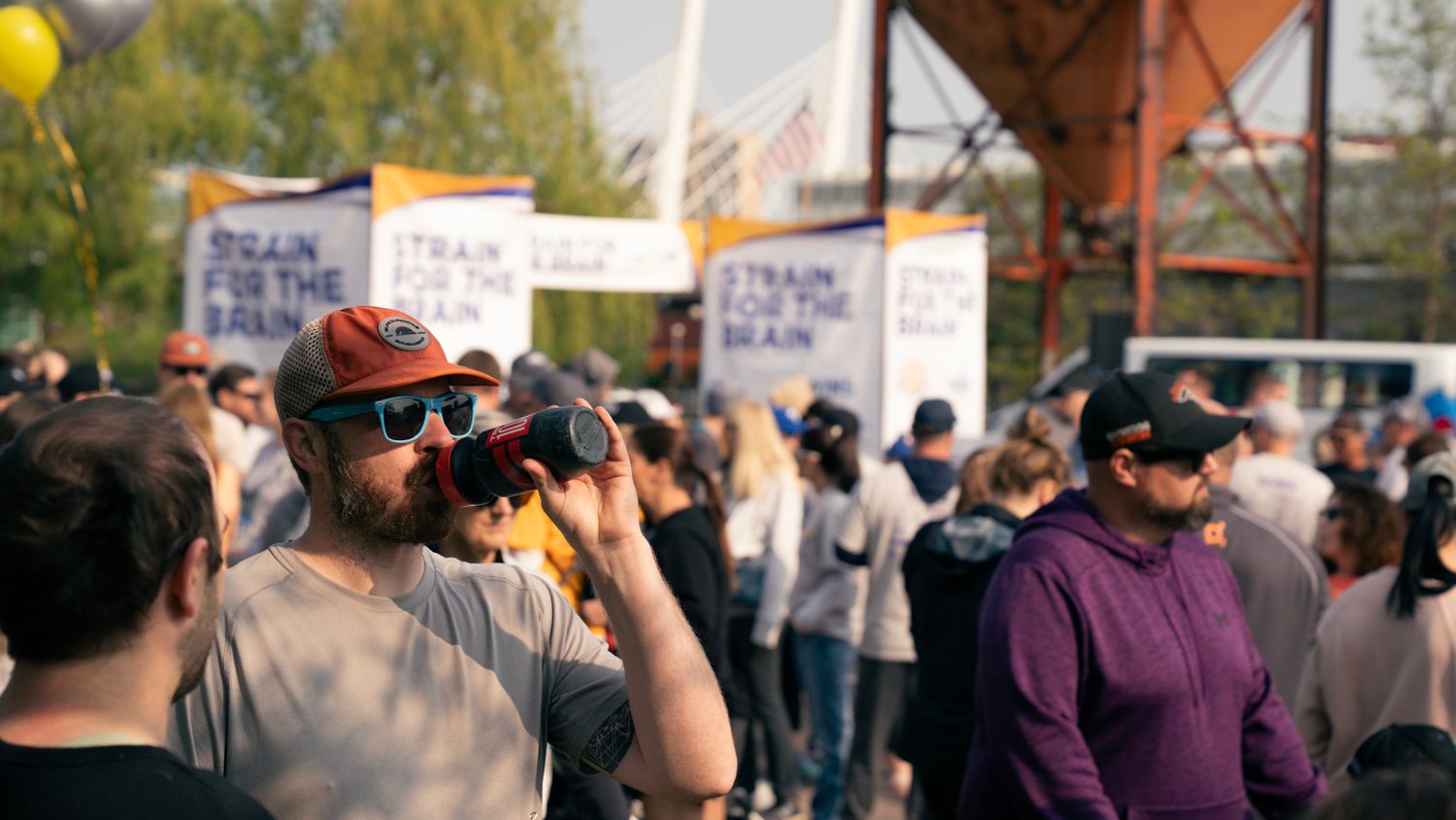 People in a crowd watching an outdoor event with yellow balloons and signs visible.
