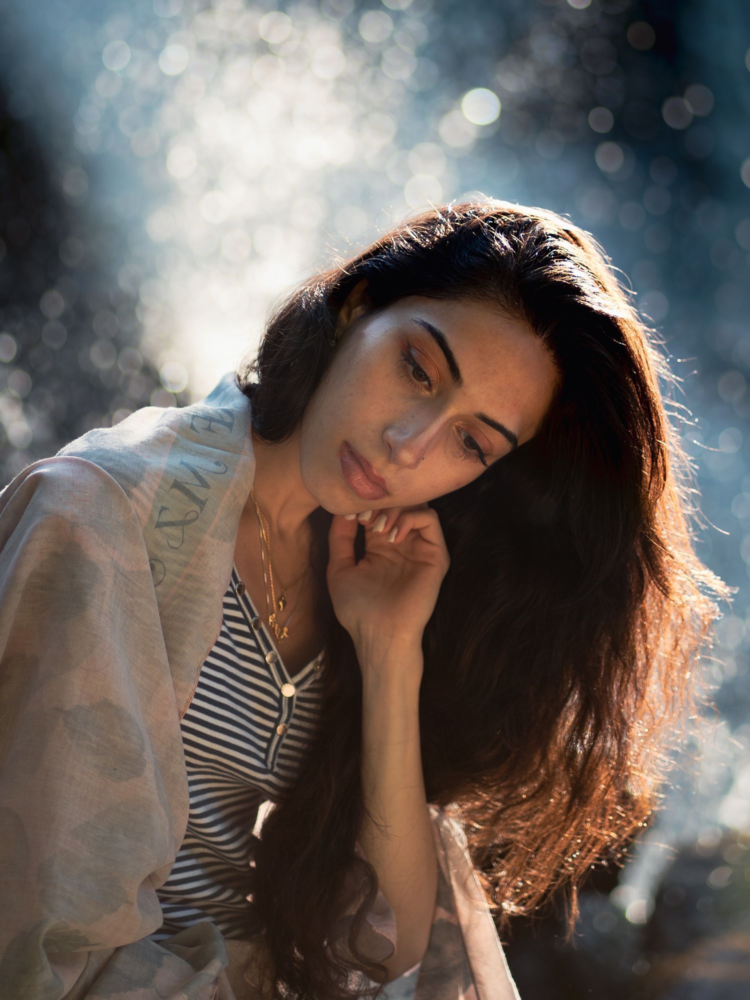 A dreamy portrait in backlit bokeh featuring long dark hair and a striped top against a soft blurred background.