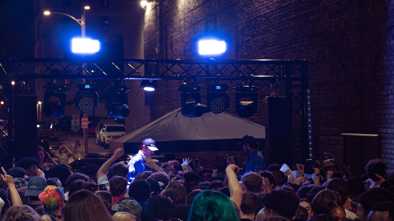 Blue stage lights illuminate a nighttime concert crowd under dark industrial architecture.