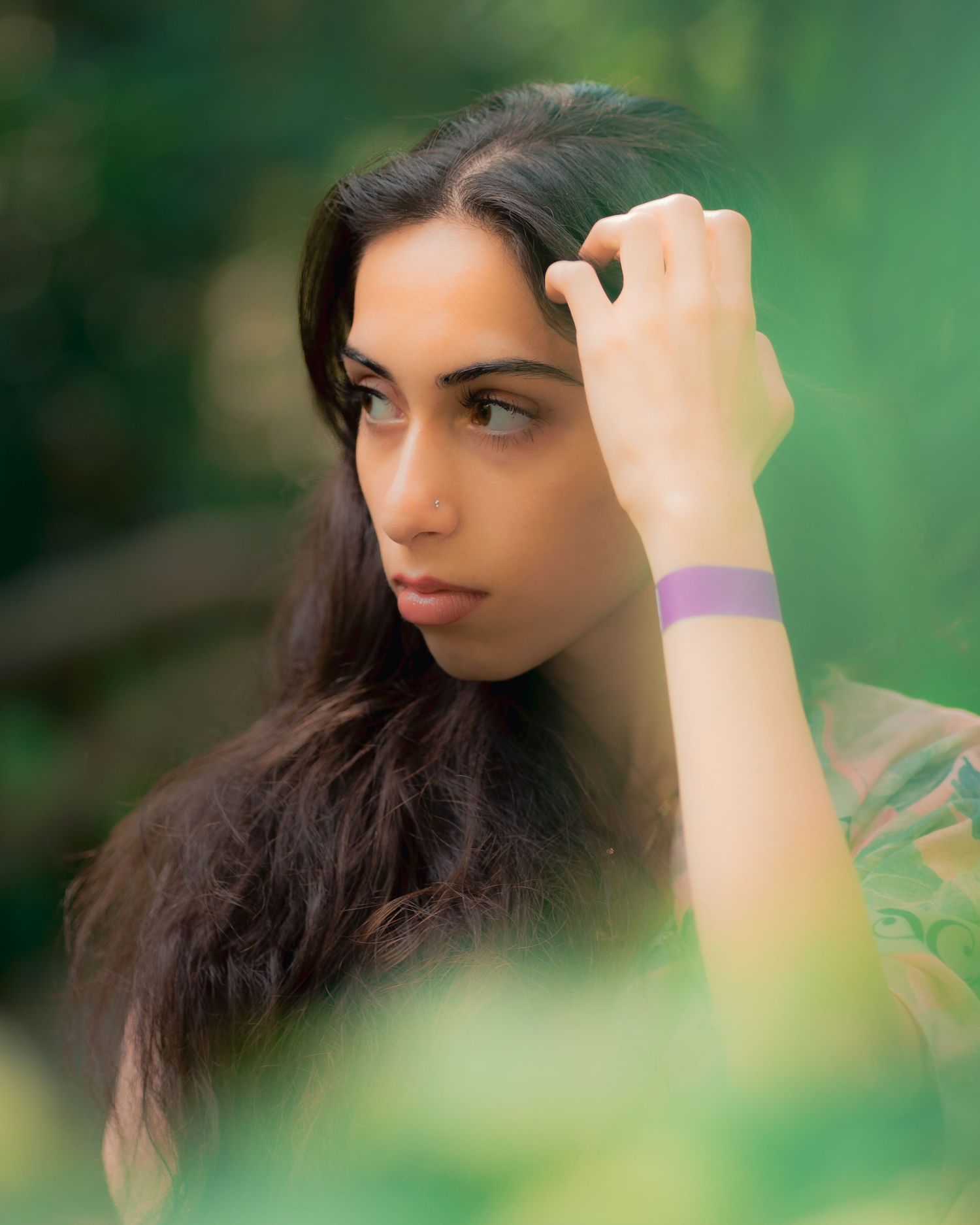Stylish person photographed in soft focus against natural green foliage backdrop in outdoor setting.