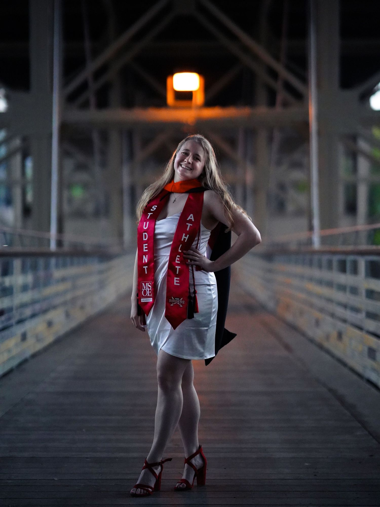 A person in a white dress with red accents poses at increasing distances on a dimly lit wooden boardwalk at dusk.